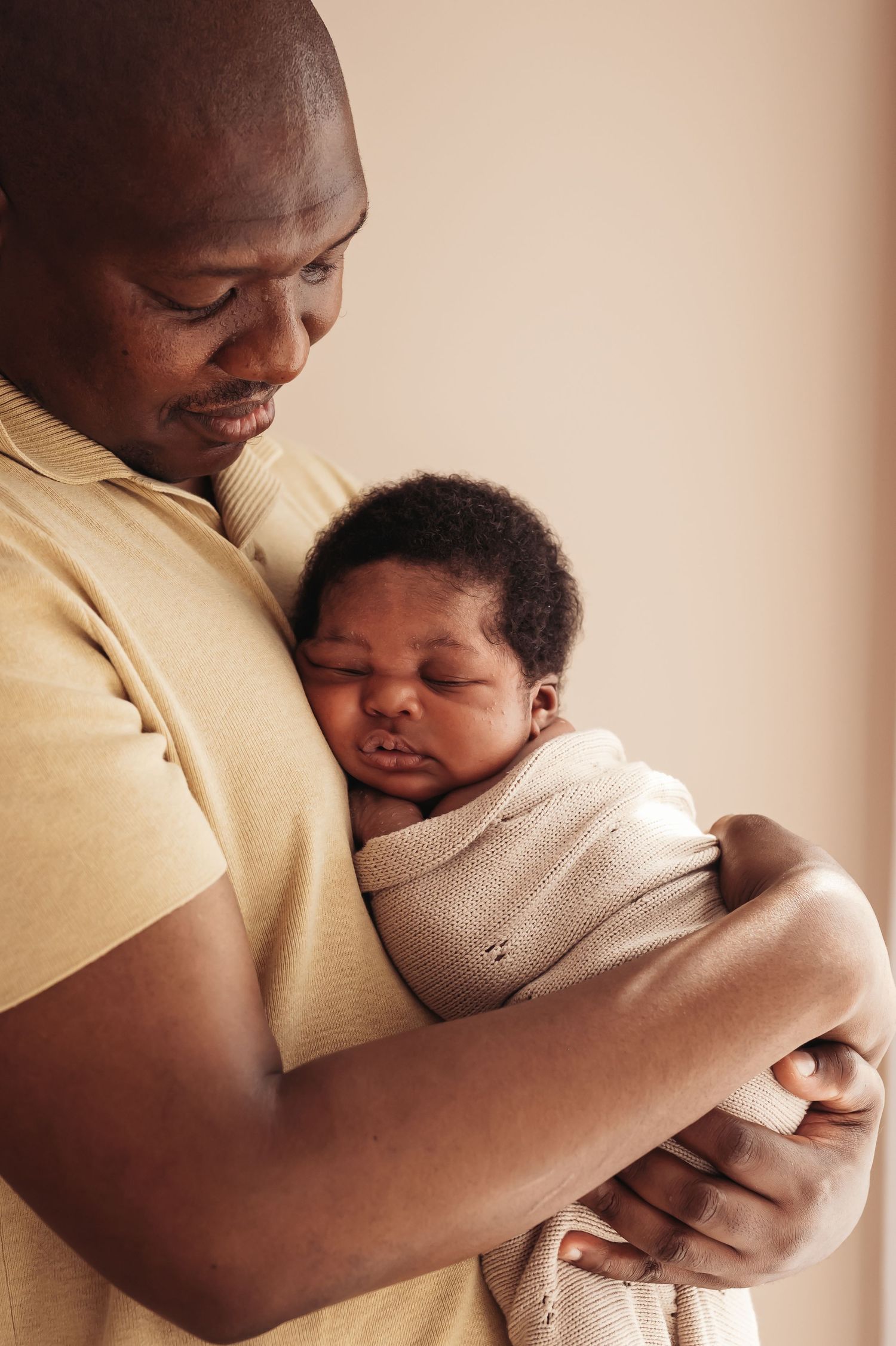 A father tenderly holds his sleeping newborn baby wrapped in a soft blanket, sharing a peaceful moment.