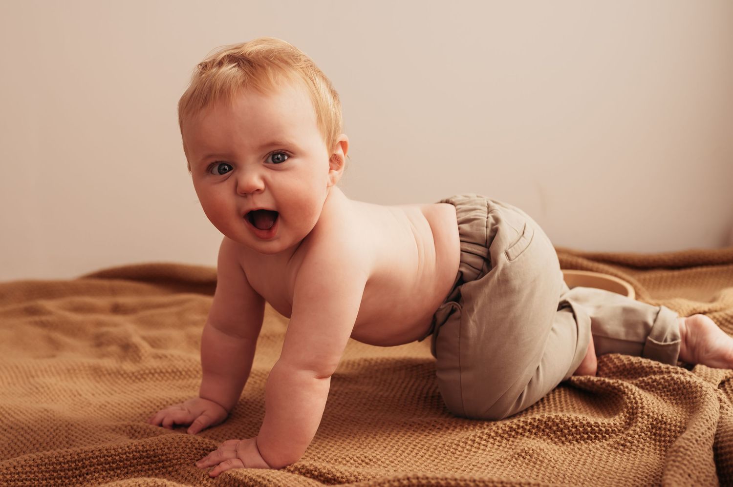 Cheerful baby crawling on brown blanket..