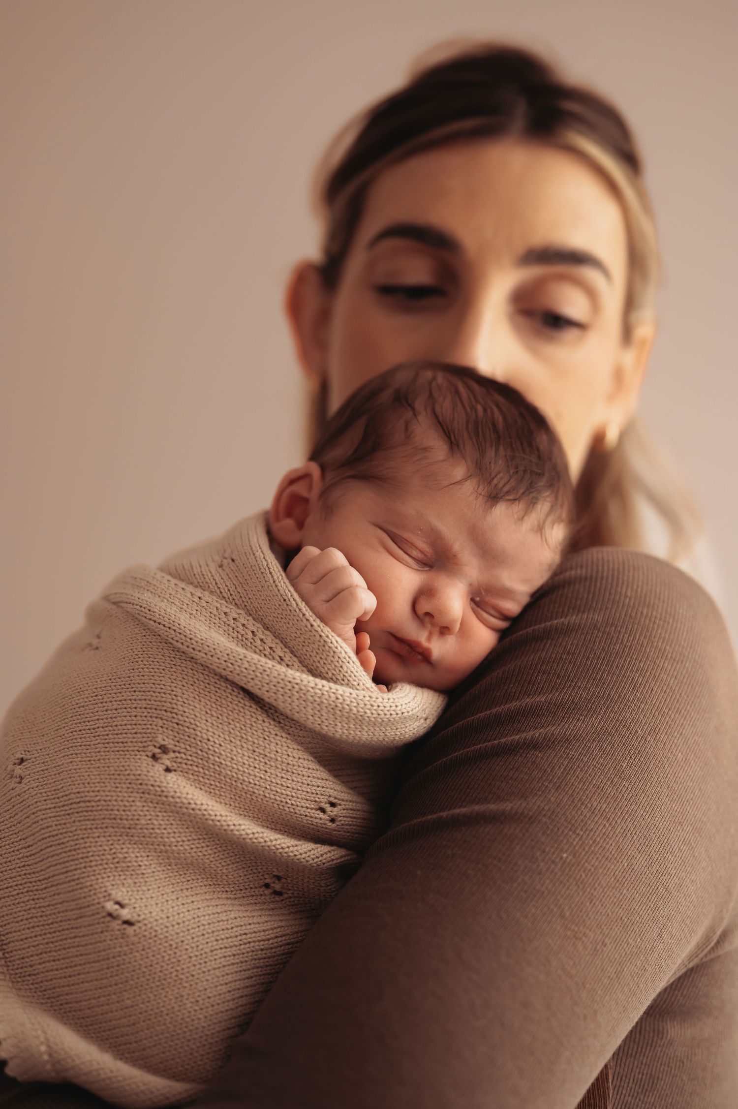 Tender moment of sleeping newborn cradled in beige wrap against mother.