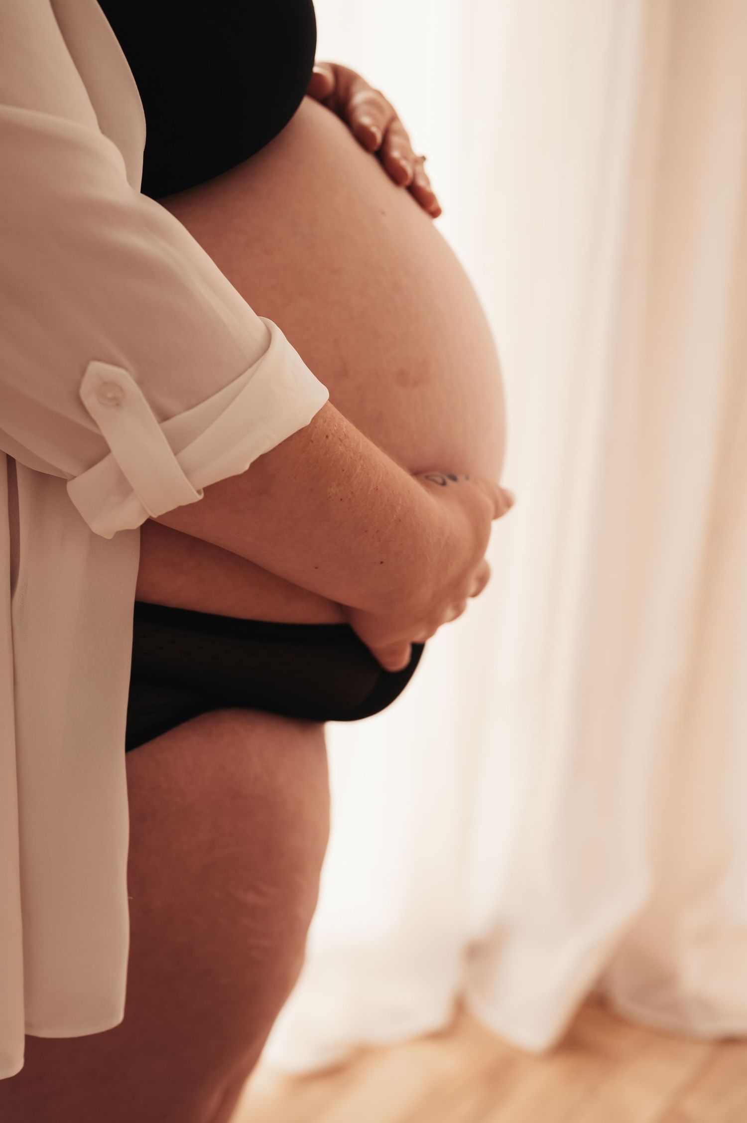 Side profile of pregnant belly with hands resting gently on bump, wearing black and white clothing.