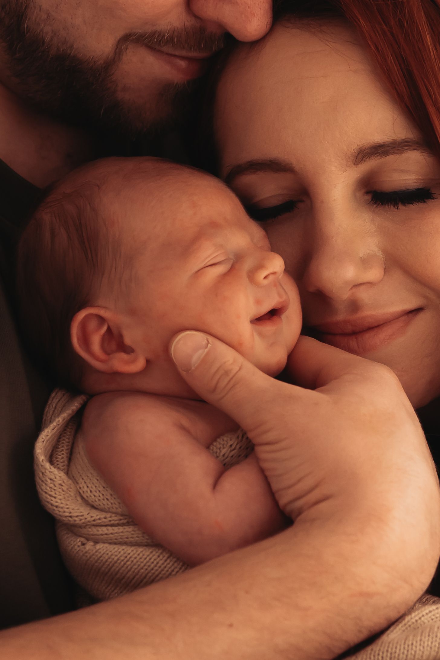 Parents tenderly holding their smiling newborn baby close, sharing a warm and loving family moment.