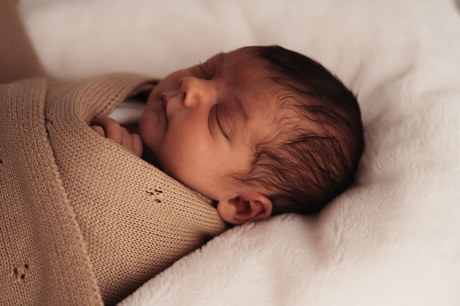 Peaceful newborn resting while wrapped in beige knitted swaddle blanket.
