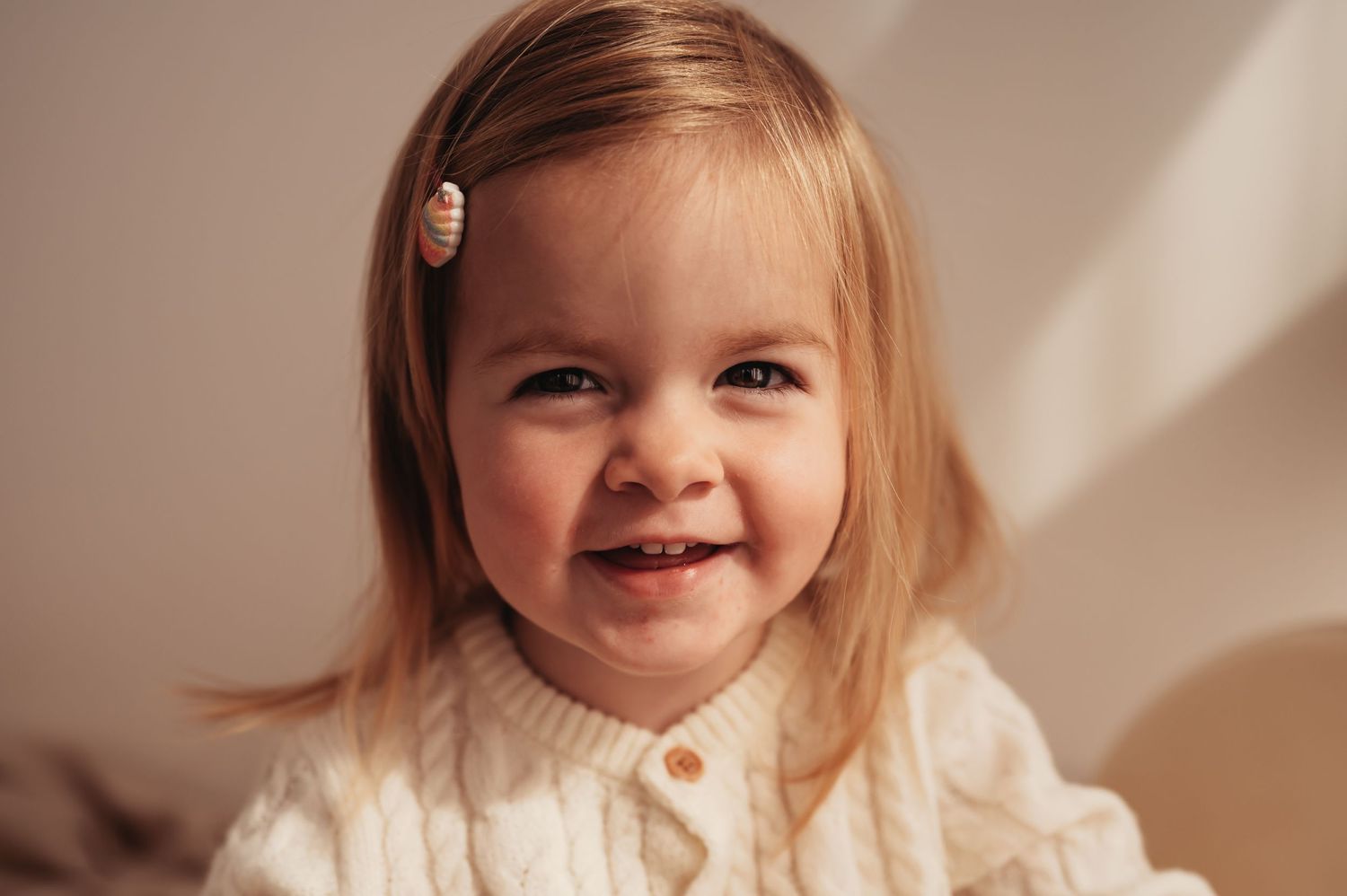 Portrait in warm tones showing bright smile and cream knit sweater.