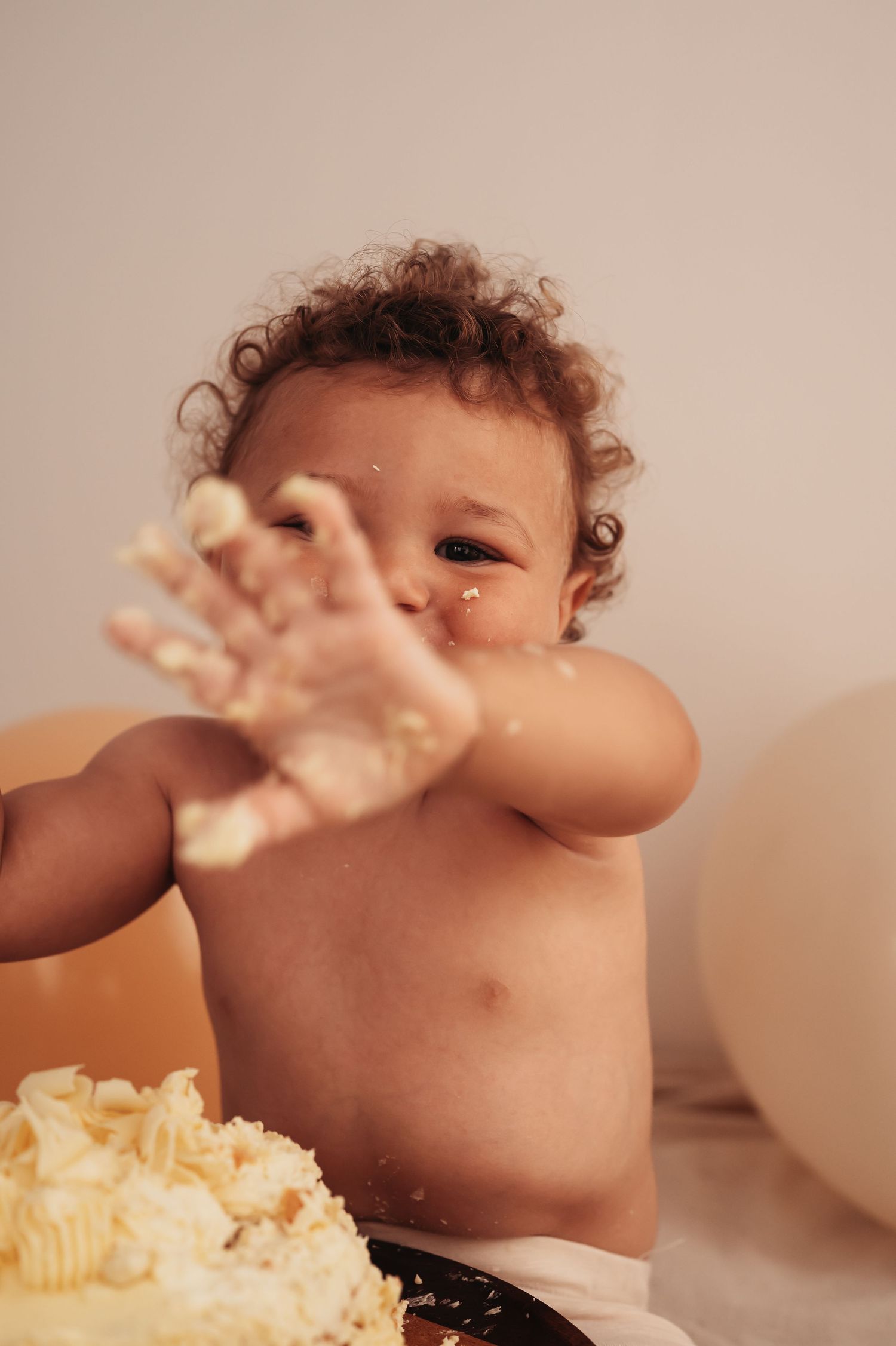 A messy baby playing with cake and frosting during a celebration.