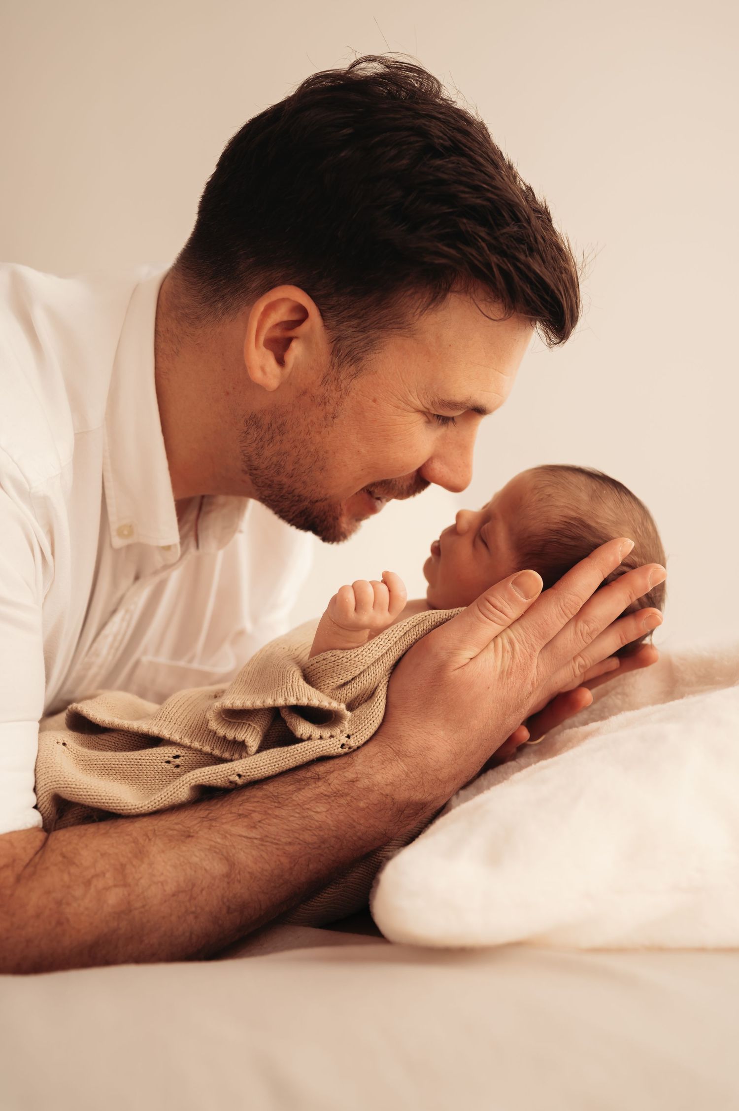 Parent sharing tender moment with swaddled newborn on white bedding.