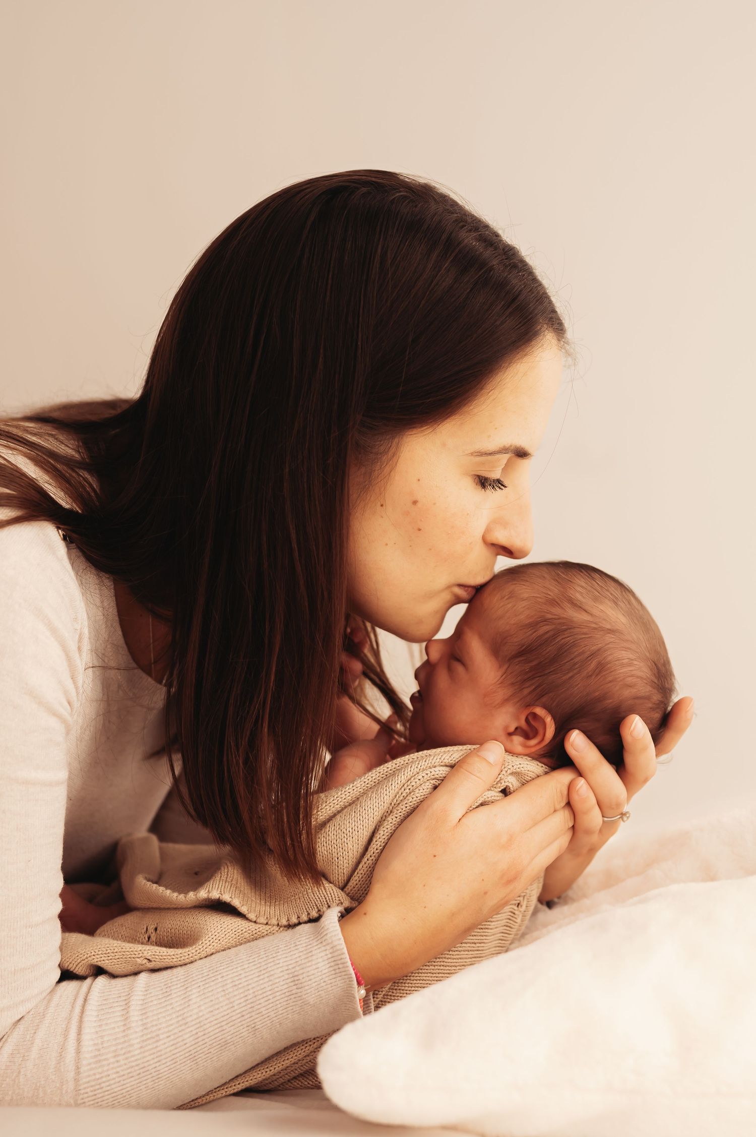 Intimate moment between mother and newborn as she gives gentle kiss on white bedding.