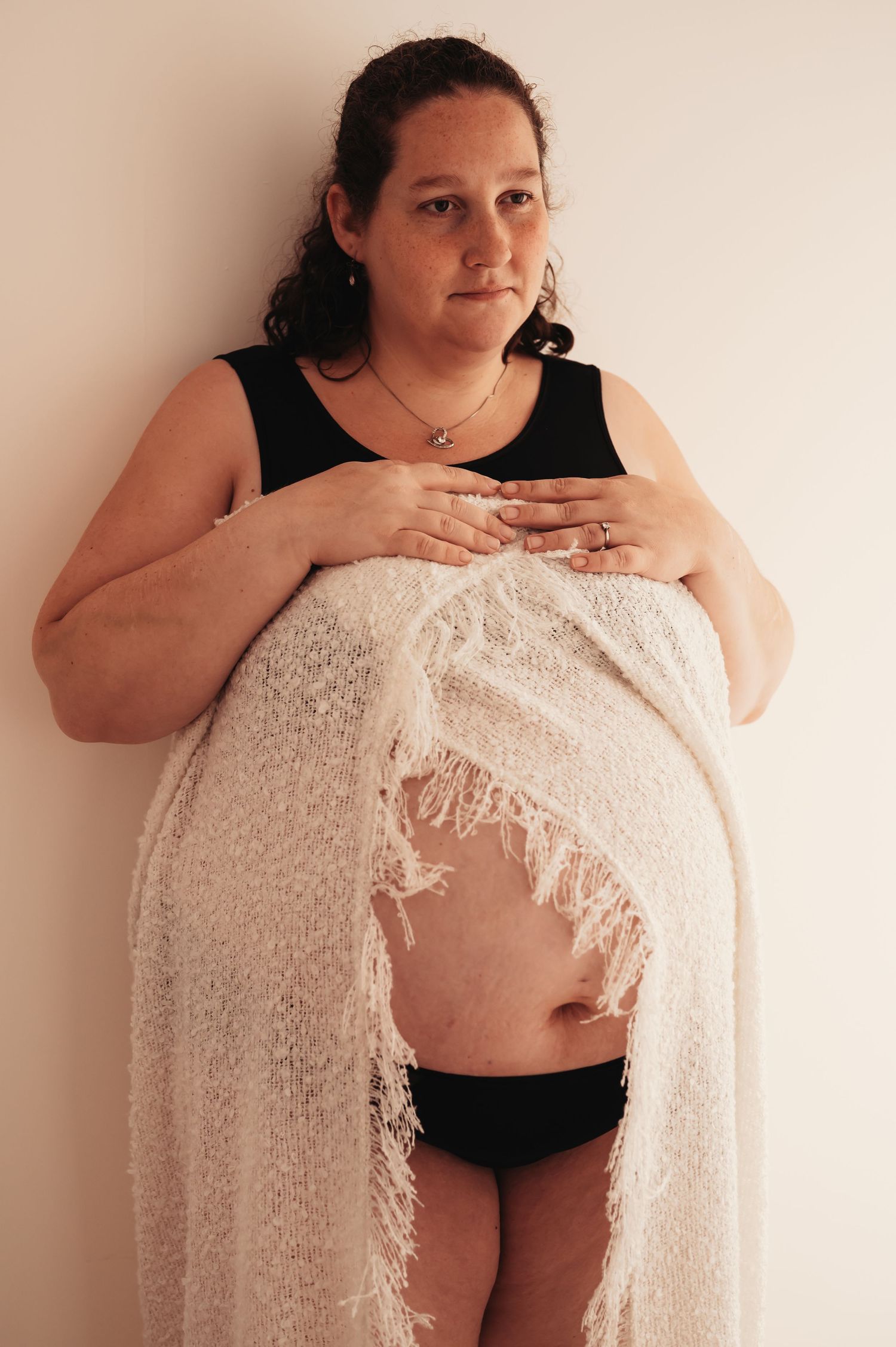 Full-length maternity photo with textured cream wrap draped over black undergarments.