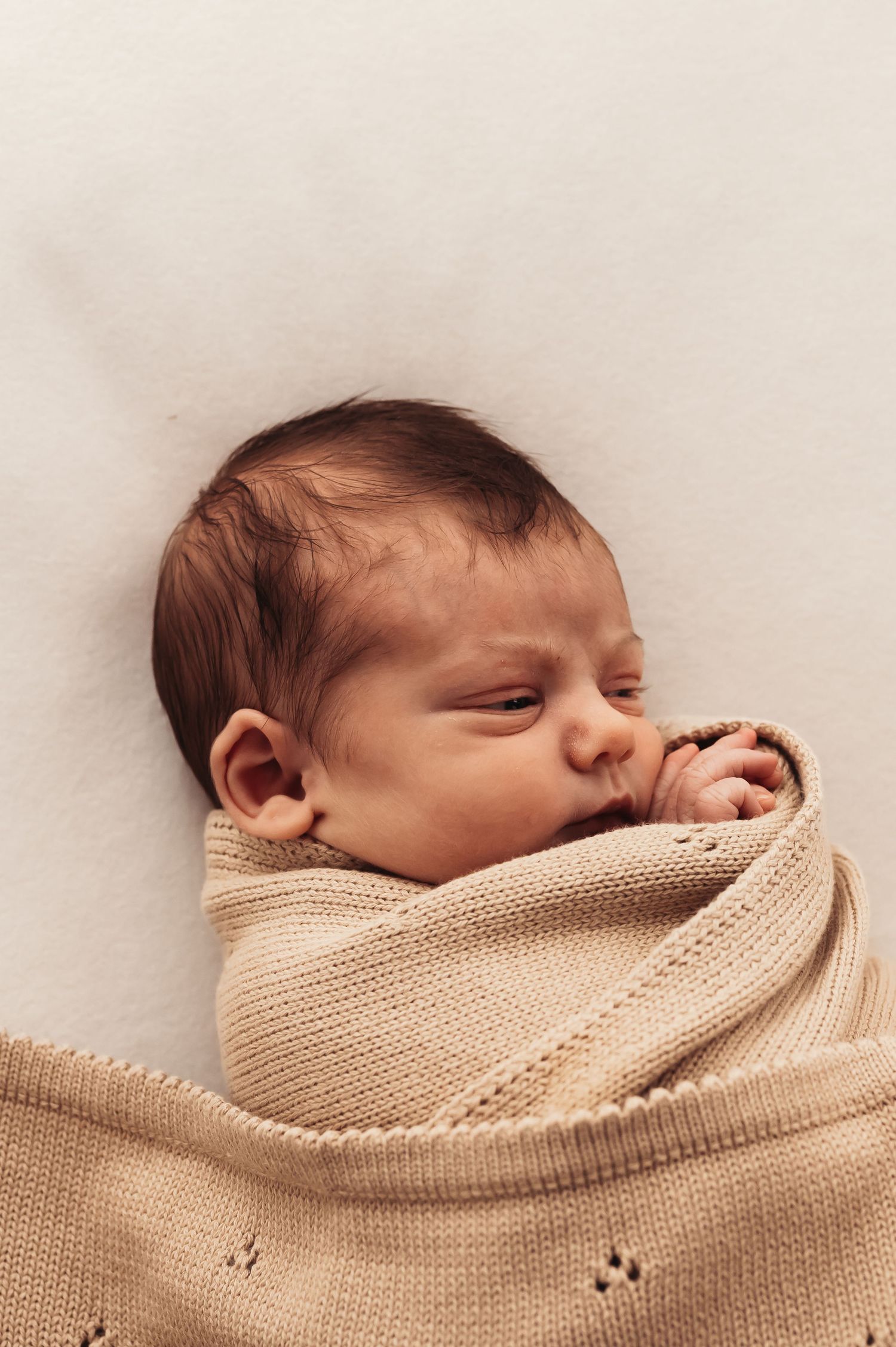 Close-up of sleeping infant wrapped in beige textured blanket against white background.