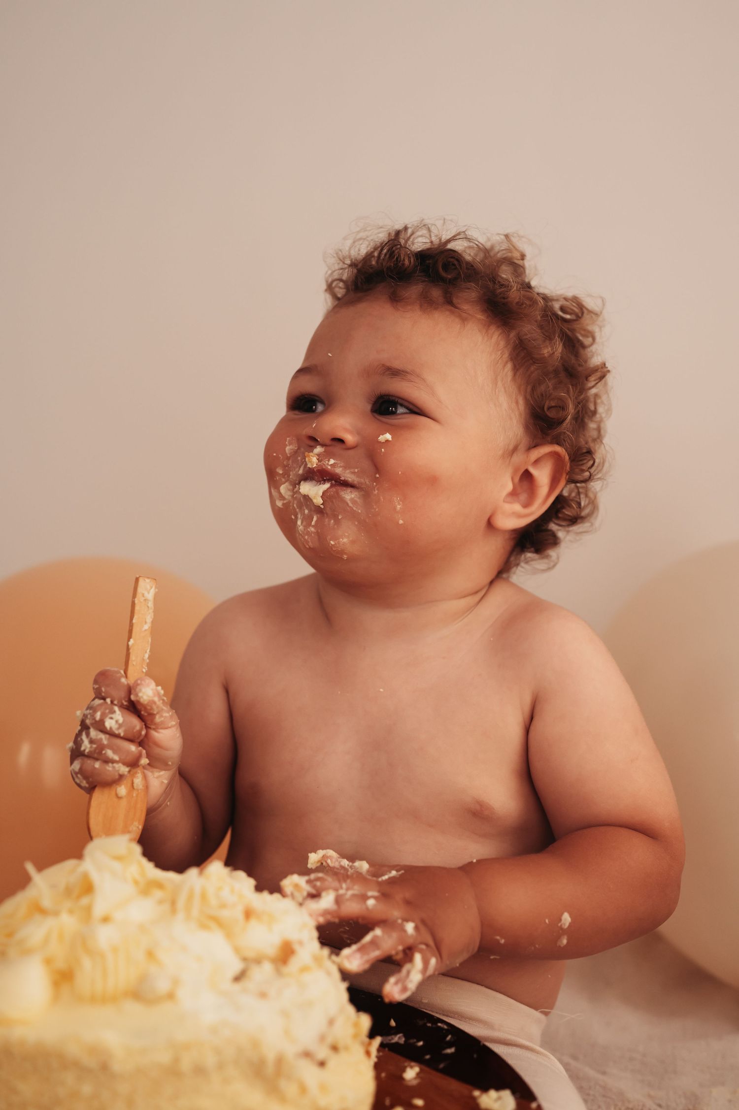 Smiling toddler enjoying cake smash photoshoot with cream frosting all over face.