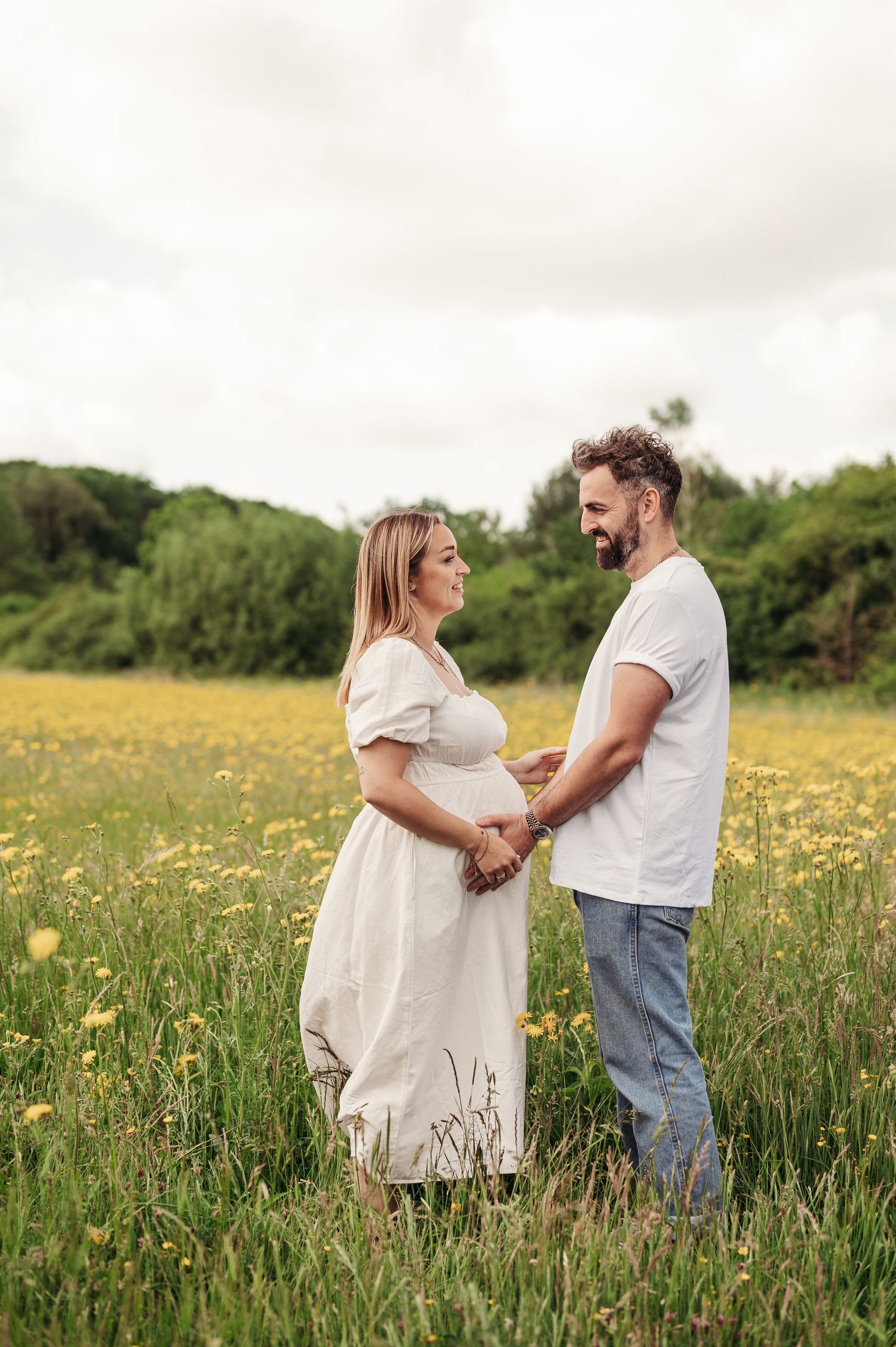 Couple standing together in a meadow of yellow wildflowers as they share an intimate moment on a cloudy day.