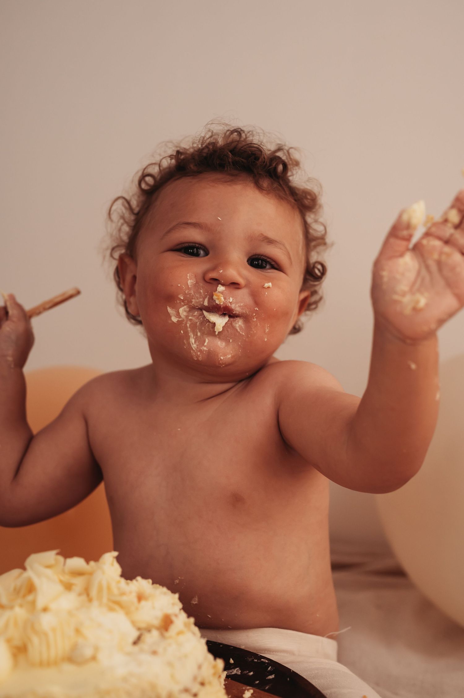 A happy baby covered in cake frosting during a cake smash photo session.