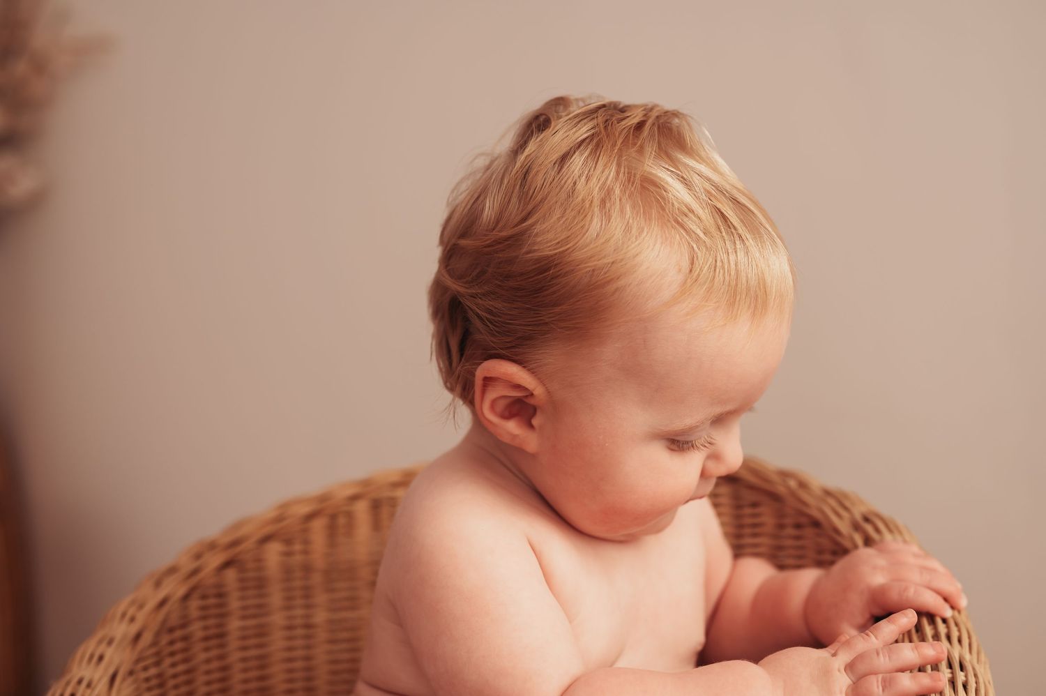 Baby in wicker chair looking down with soft lighting.