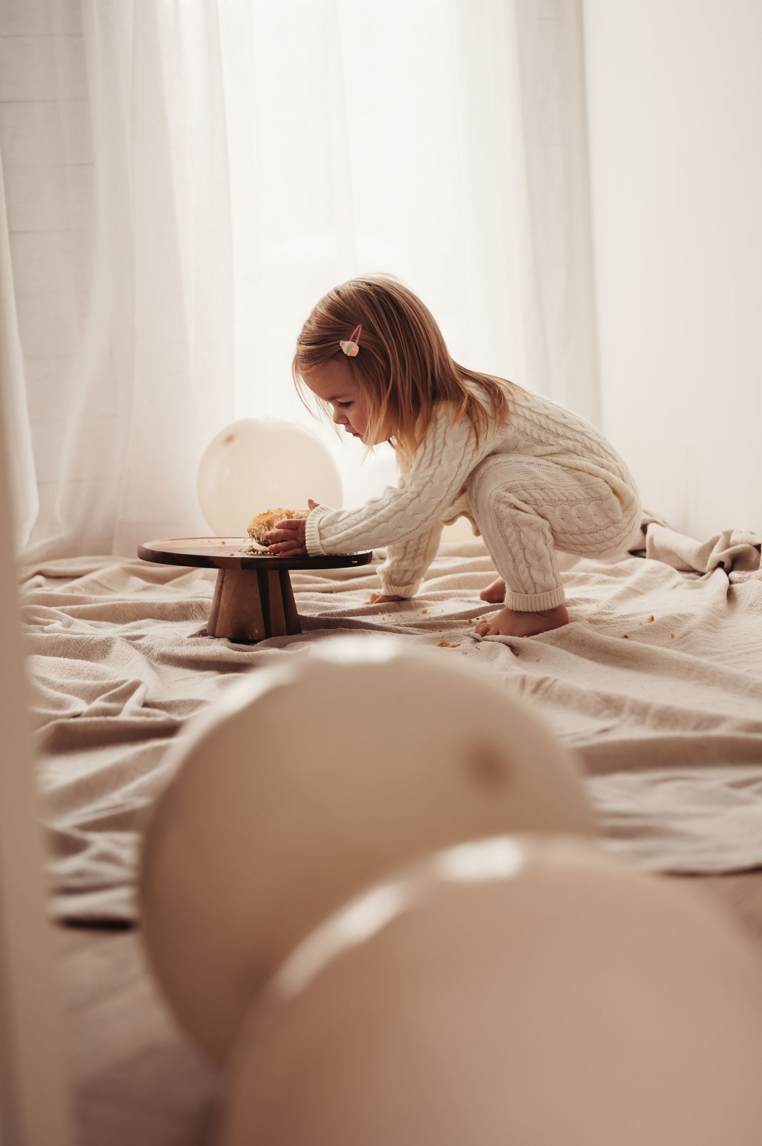 A small child in cream-colored outfit reaching across for cake.