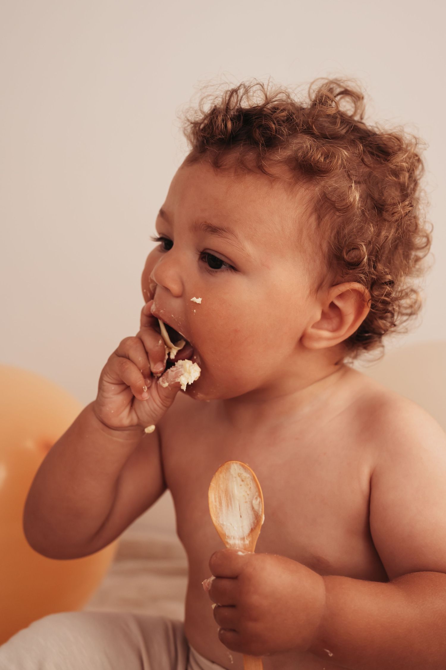 Happy toddler eating cake with frosting on face during first birthday photoshoot.