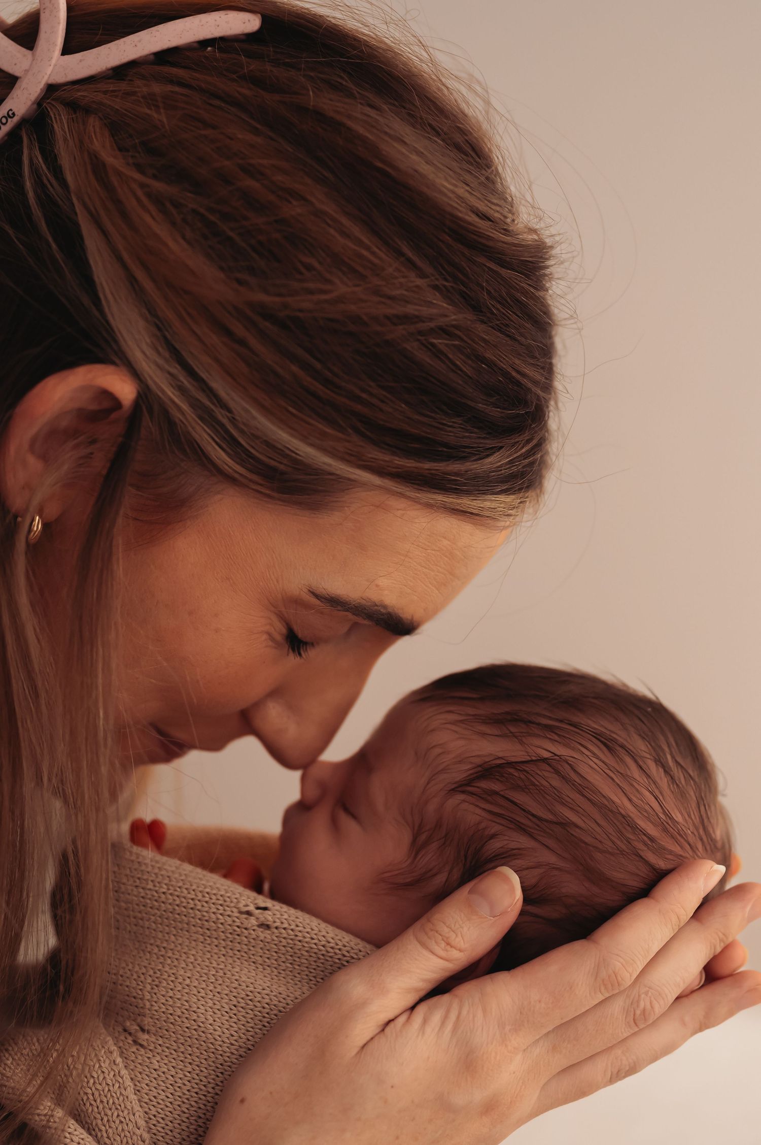 Intimate portrait of mother holding sleeping newborn wrapped in knit blanket.