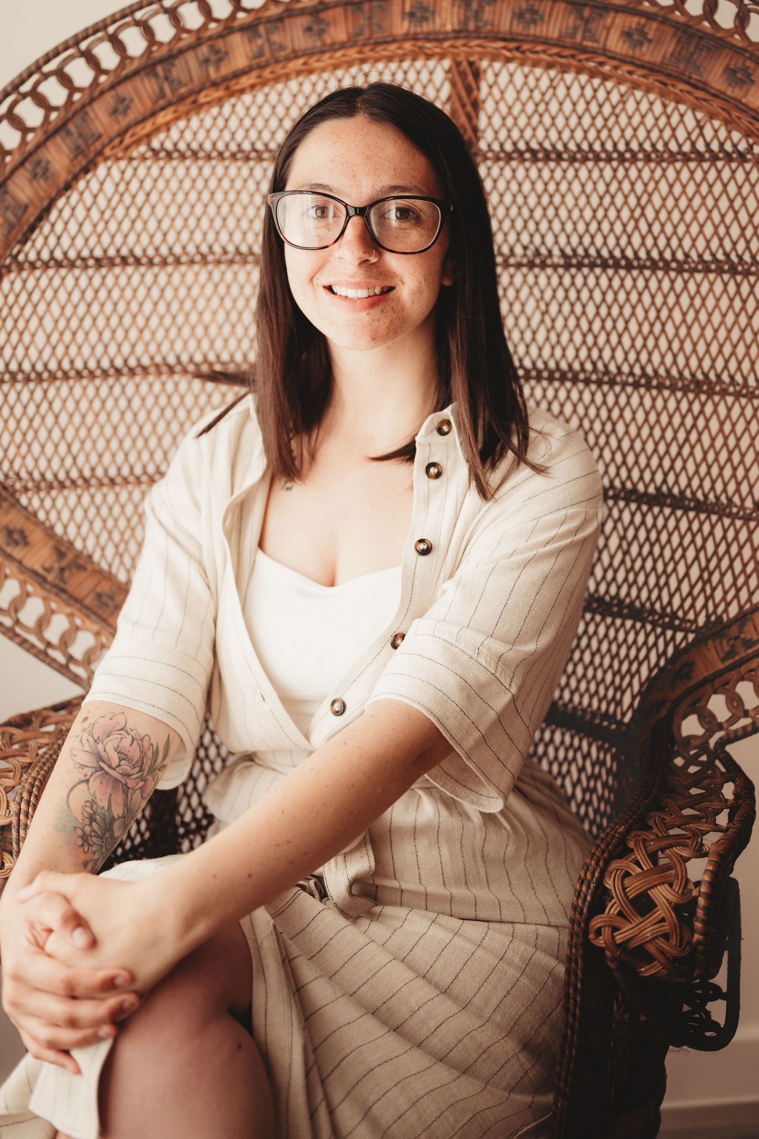 A self-portrait of owner in glasses and striped outfit poses on a wicker peacock chair.