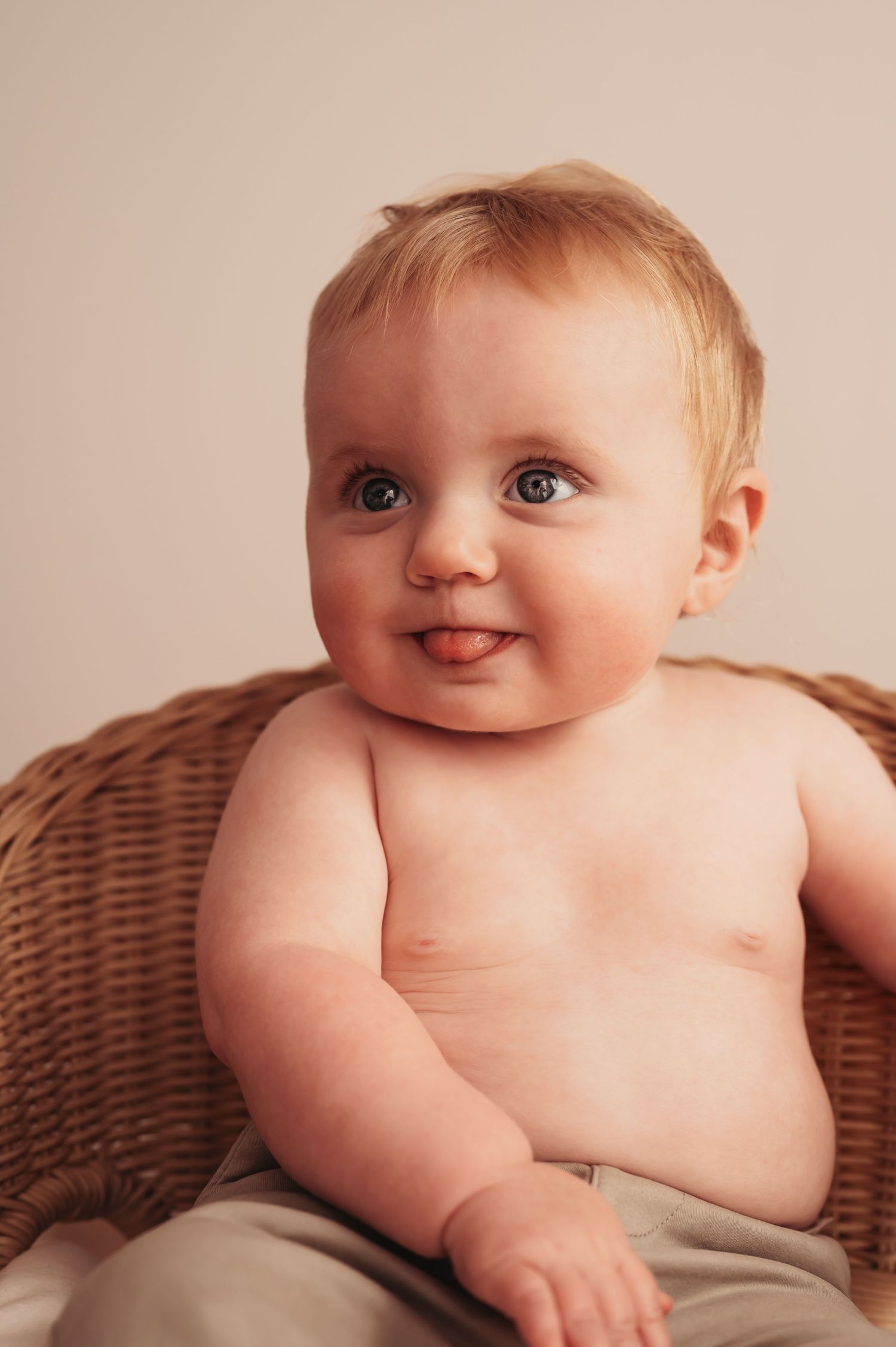 Smiling baby poses in wicker chair during portrait session.
