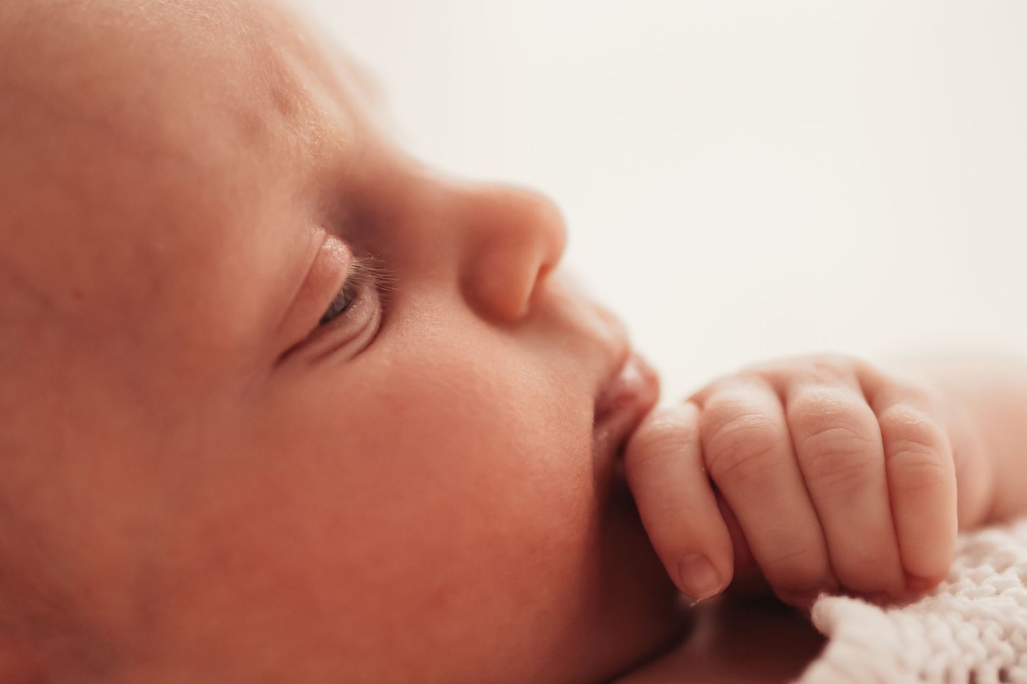 A close-up profile view of a sleeping infant's face with tiny hand near mouth.