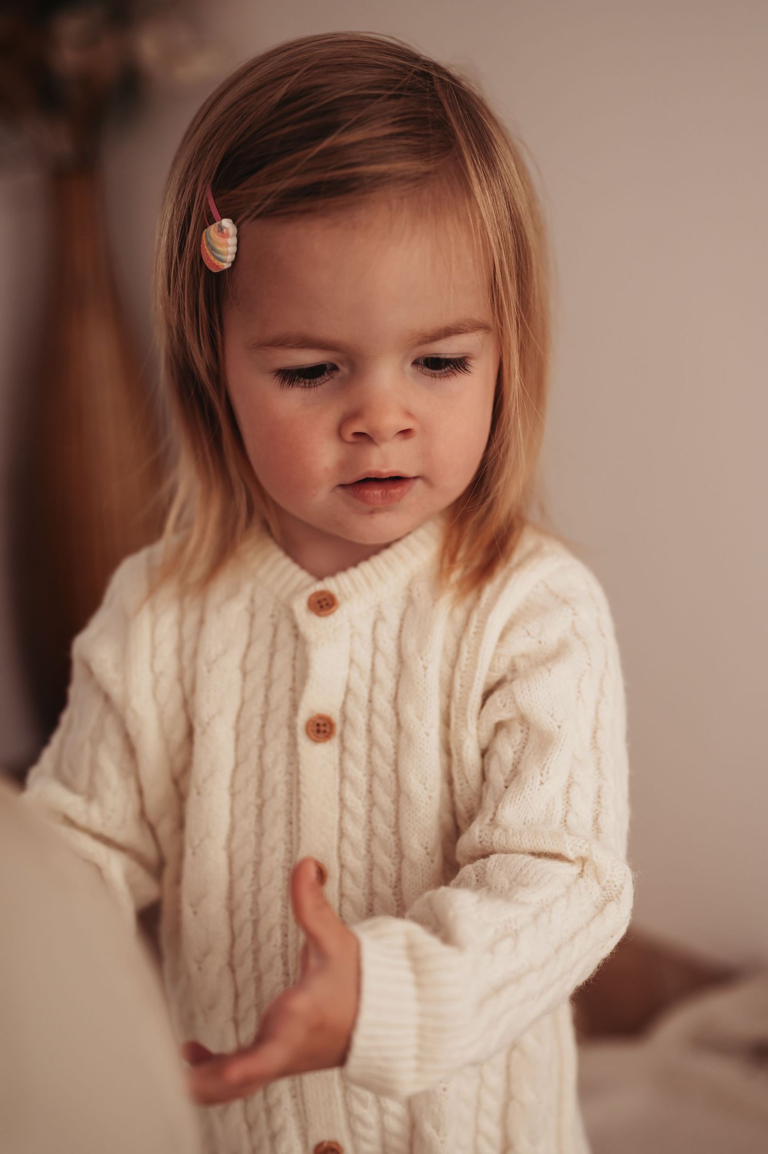 Close up of young person in cream cable knit cardigan with hair clip in soft lighting.