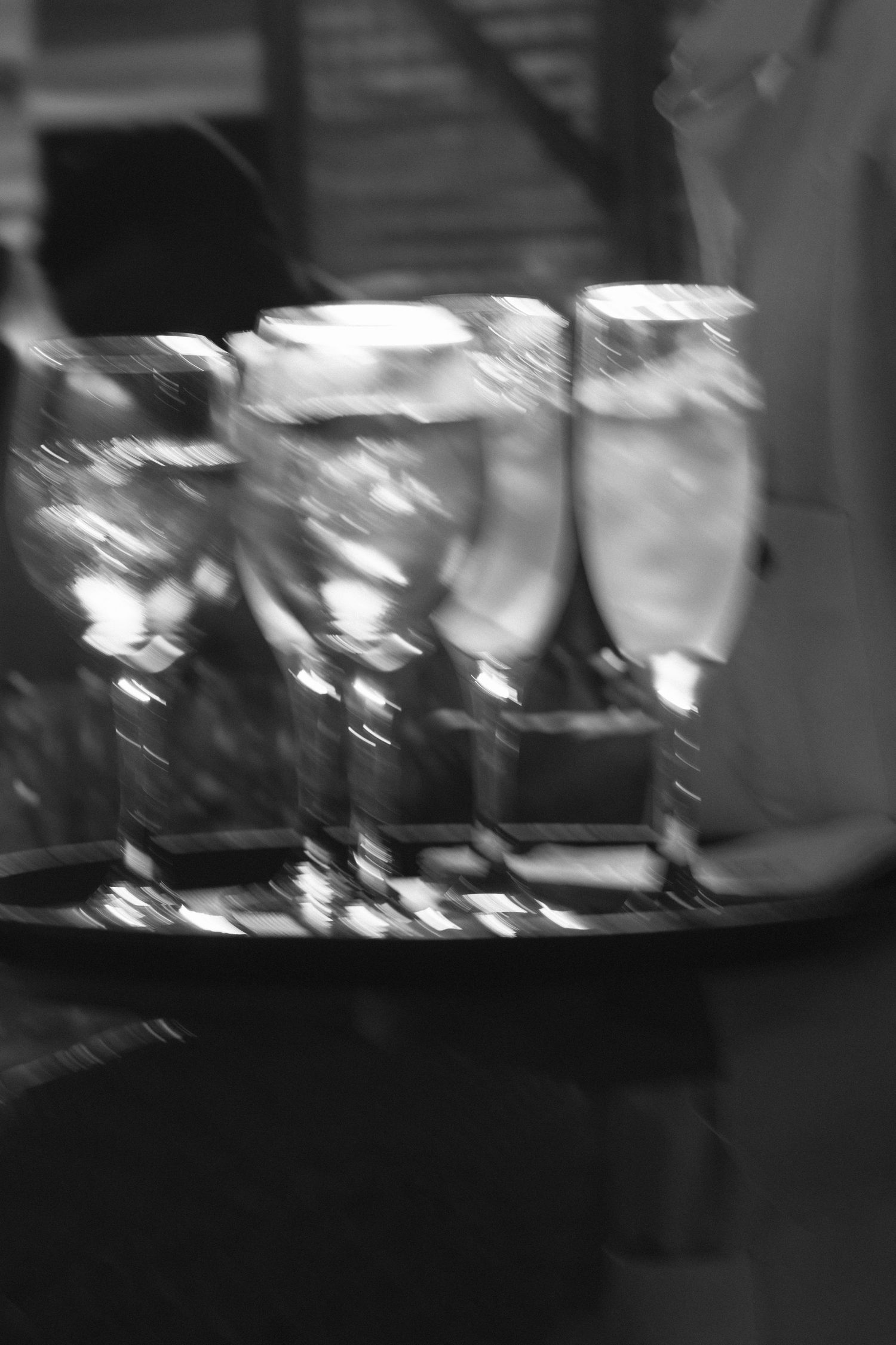 Several wine glasses filled with white liquid cocktails are arranged on a dark surface in black and white.
