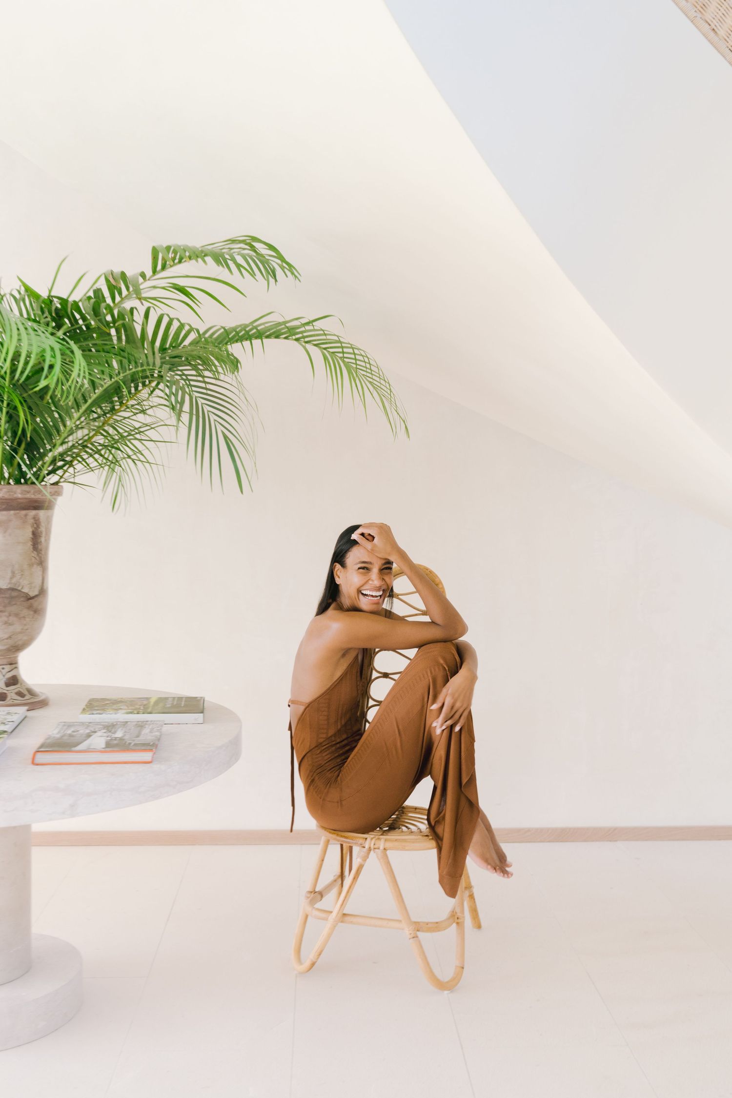 Someone sits in a rattan chair wearing a brown outfit against a white minimalist background in progressive poses.