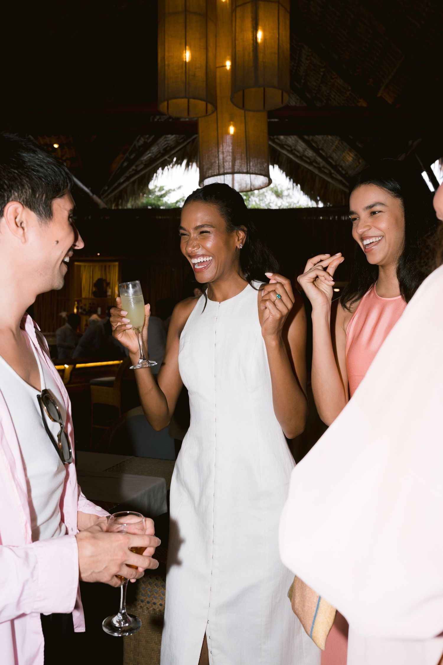 People enjoying drinks and conversation at a social gathering with elegant chandeliers and warm lighting.