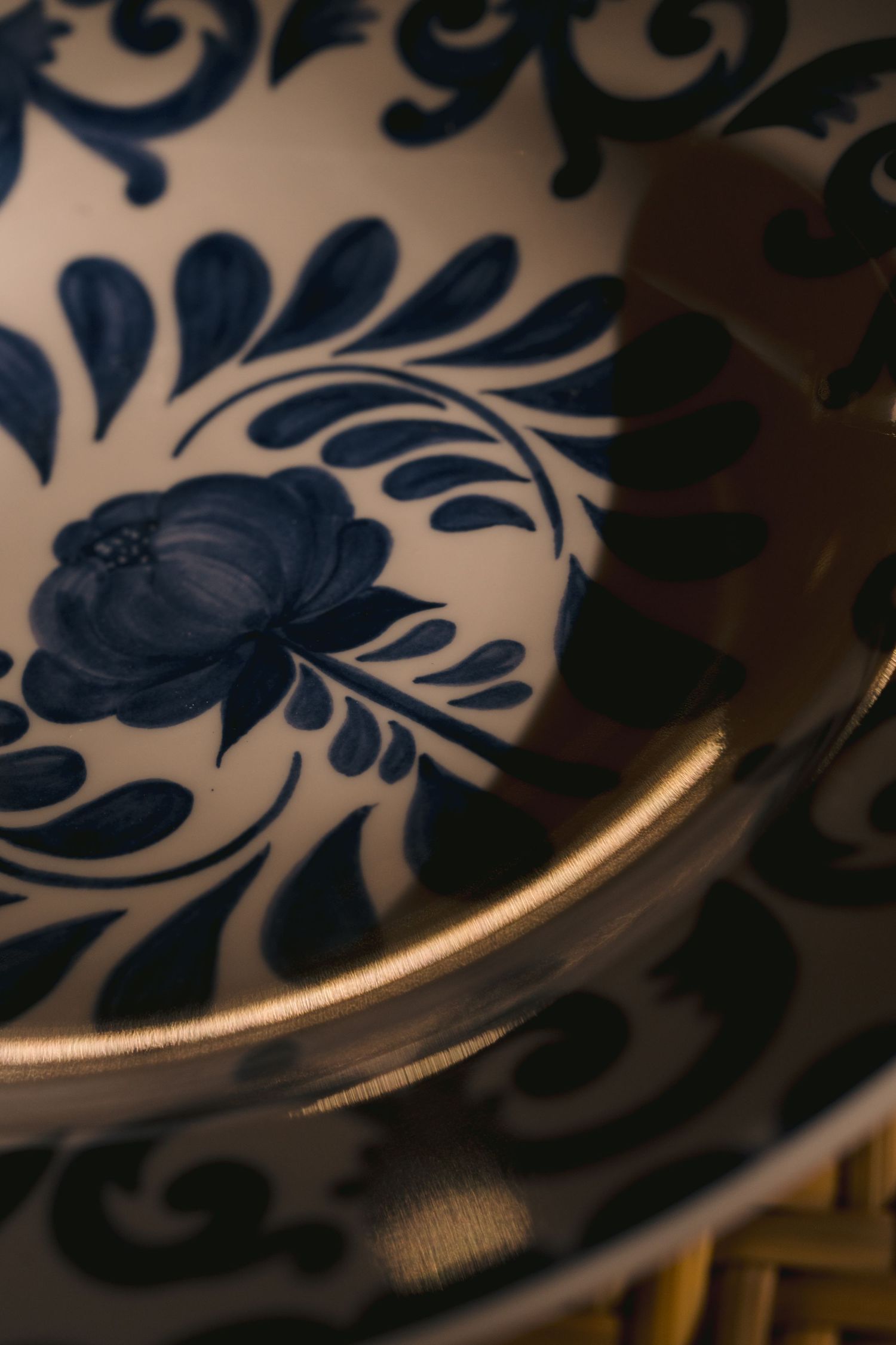 Close-up detail of blue and white porcelain dish with delicate floral pattern and gold trim along the edge.