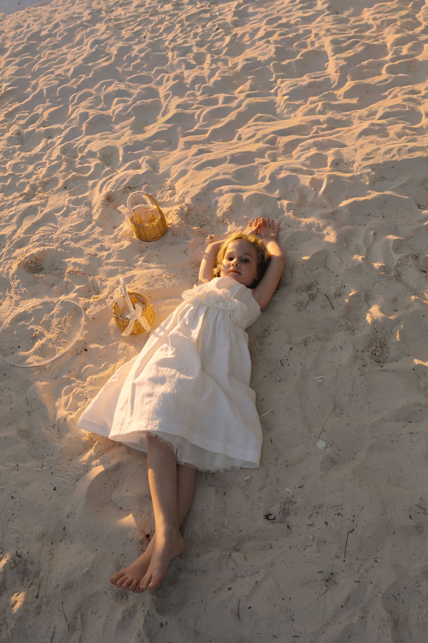 A person in a white dress lies peacefully on a sandy beach with starfish decorations at sunset.