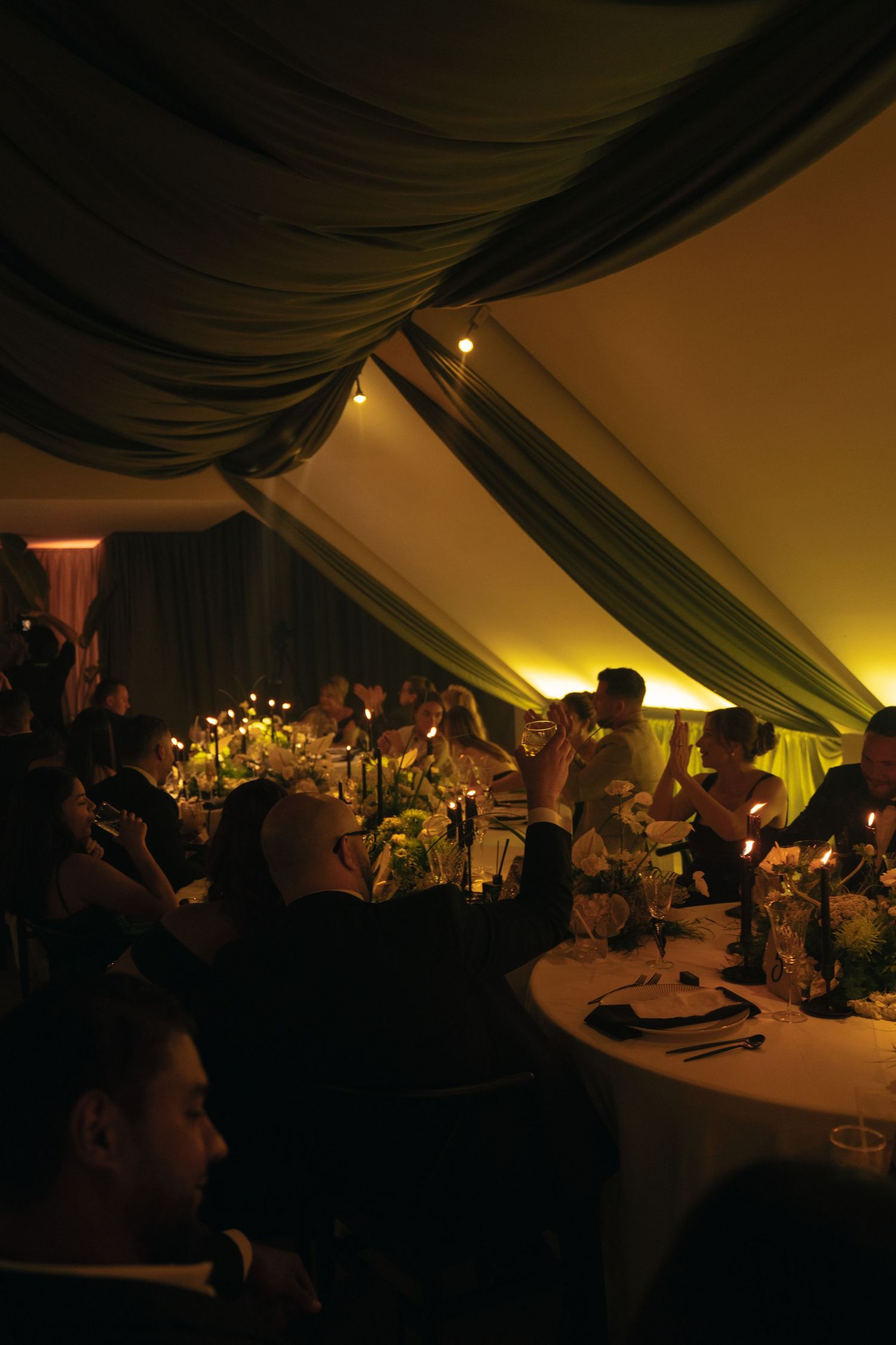 Dimly lit wedding reception under tent with floral centerpieces and ambient lighting.