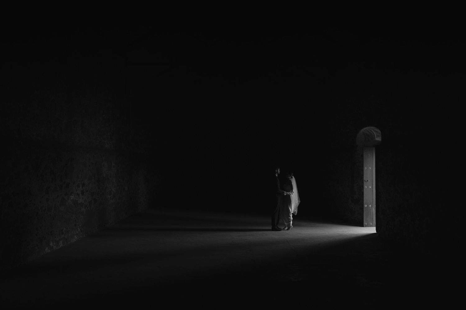 A silhouetted figure stands in a dark hallway illuminated by distant light.