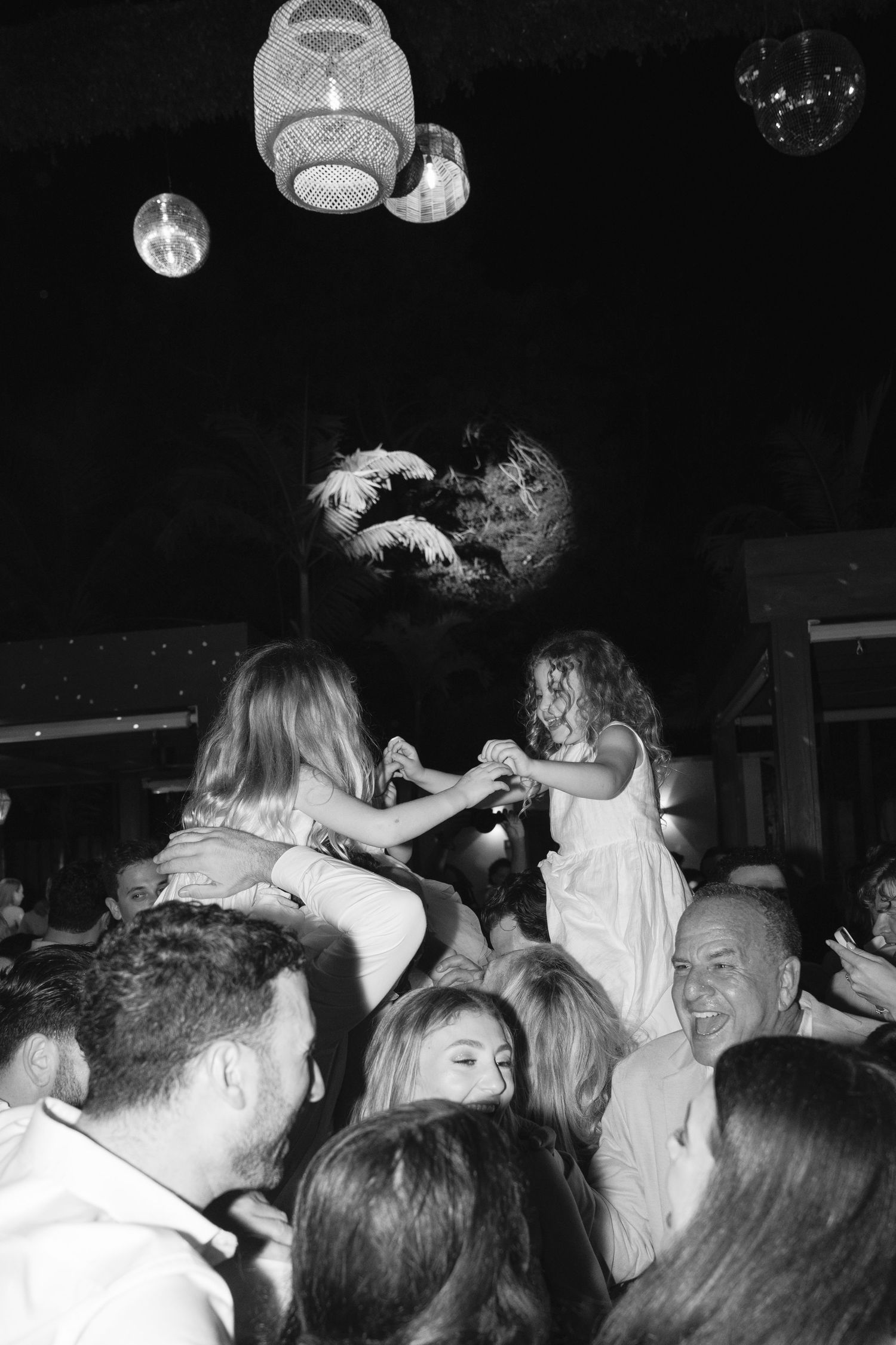 Black and white photo of a crowded party scene with paper lanterns overhead and people dancing and celebrating.