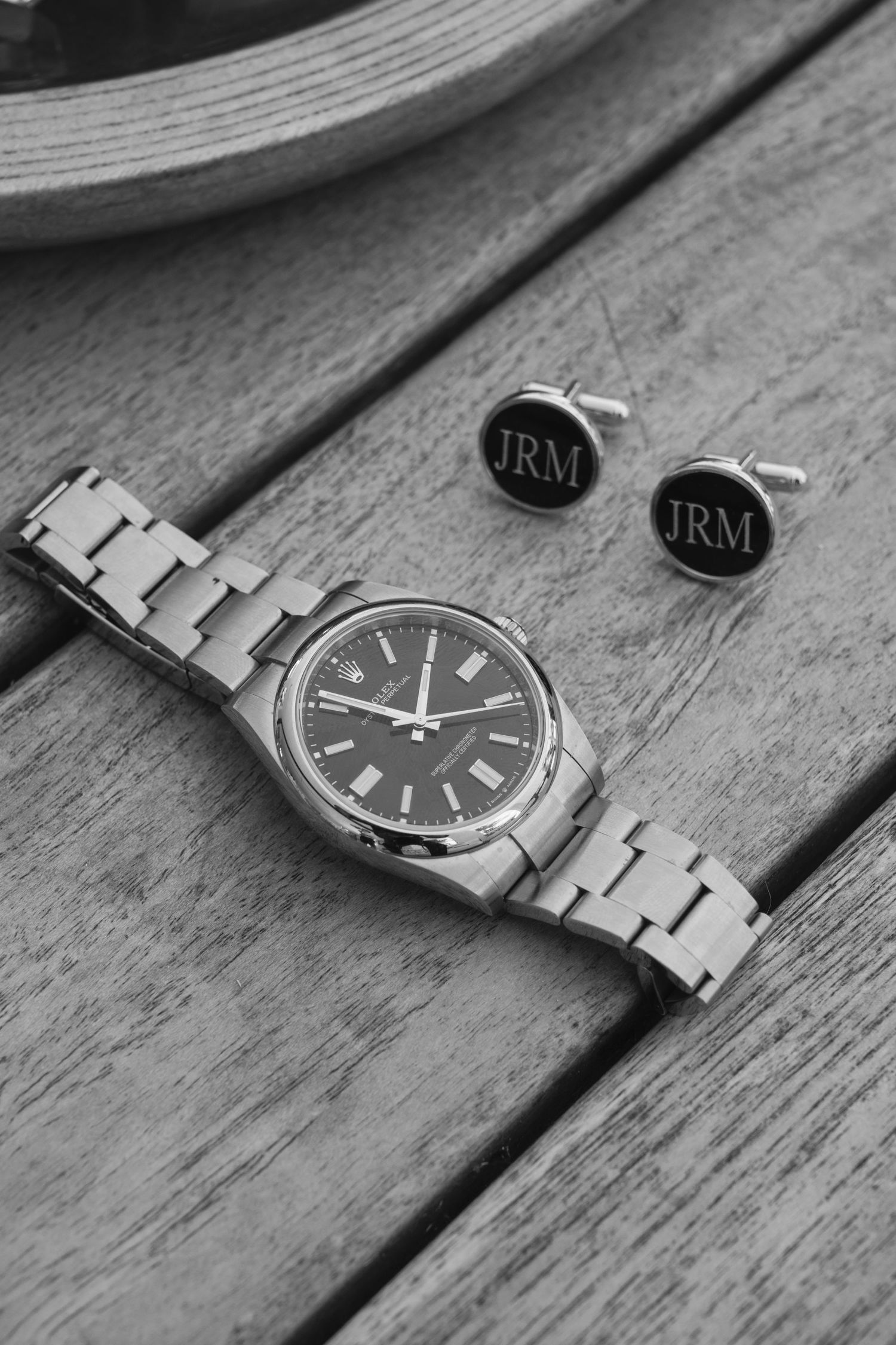 Silver metal watch and black monogrammed cufflinks with JRM initials displayed on wooden surface in black and white.