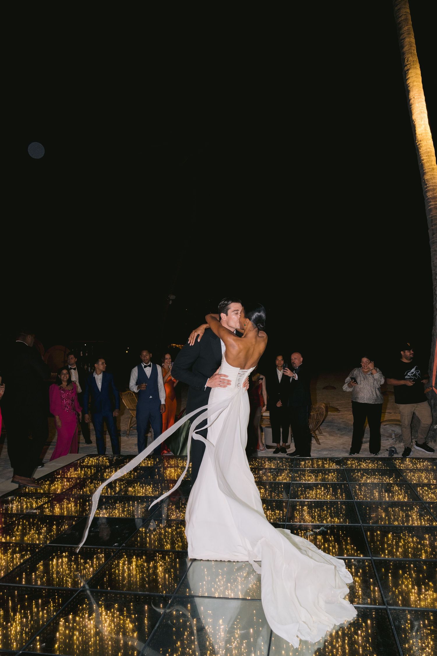 A couple embraces during their first dance at a nighttime wedding reception with candlelit steps glowing behind them.