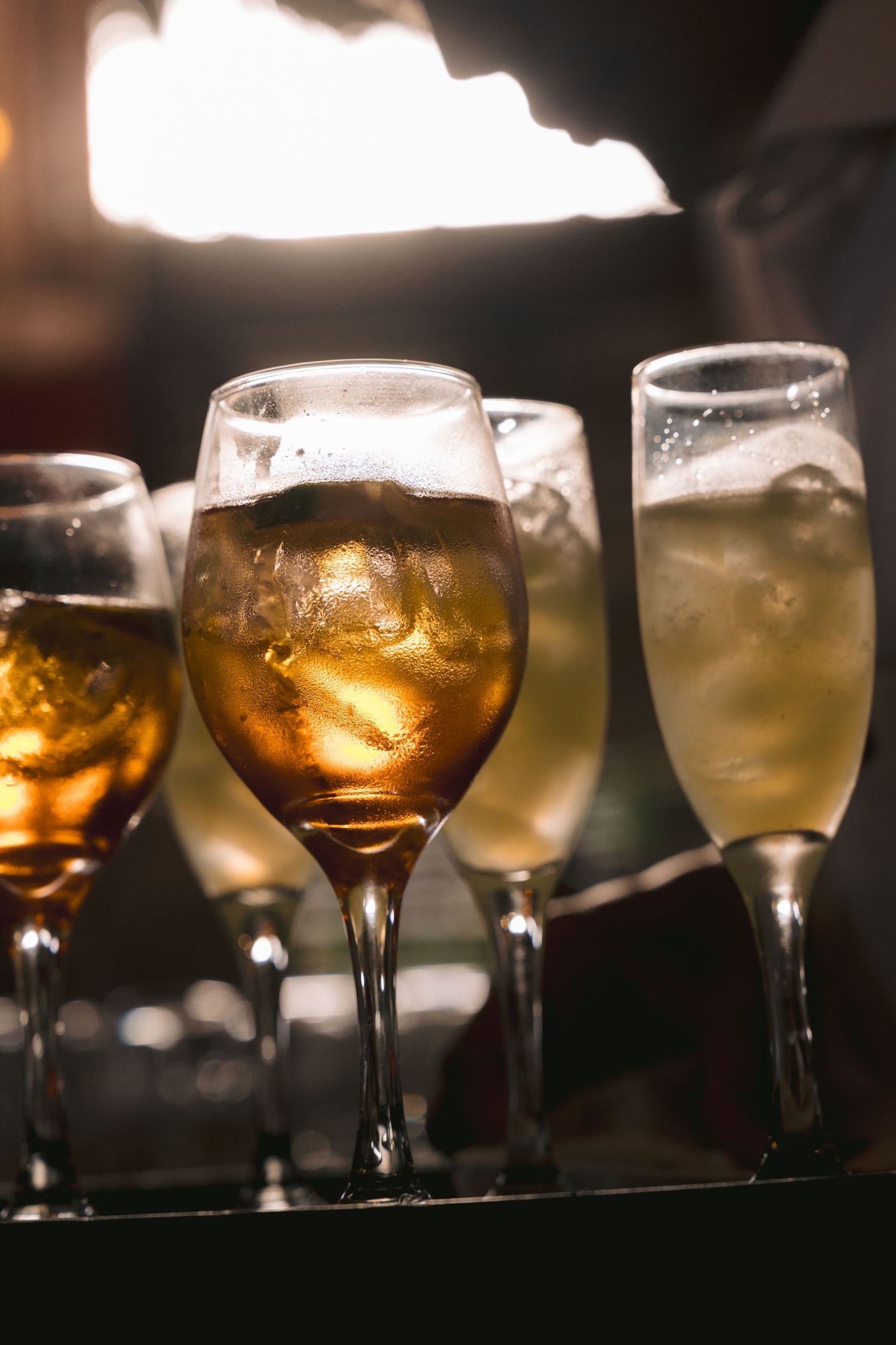 Backlit wine glasses arranged in a row create a warm amber glow against a dark background.