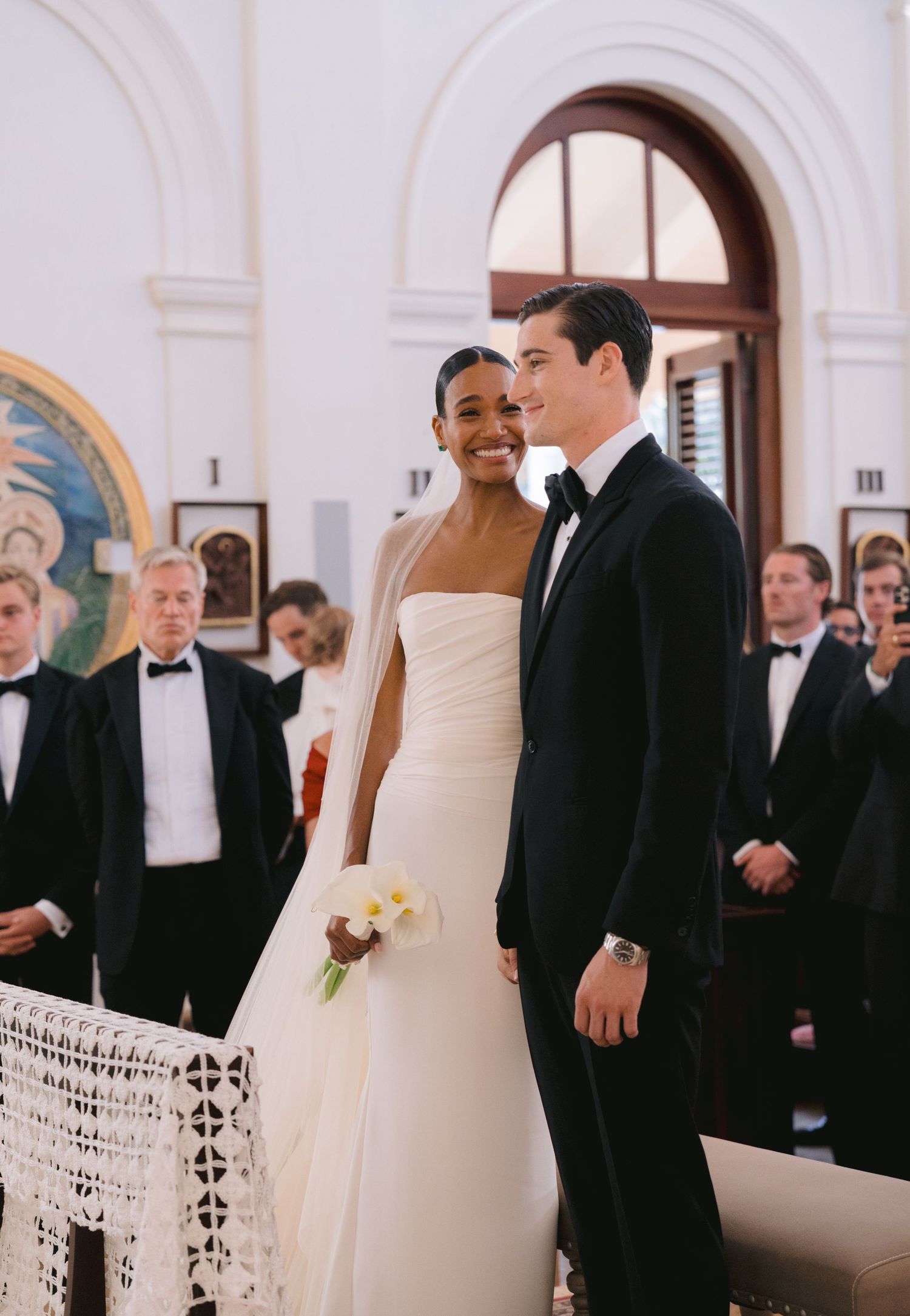 Couple in formal wedding attire share a joyful moment at the altar while guests look on in formal dress.