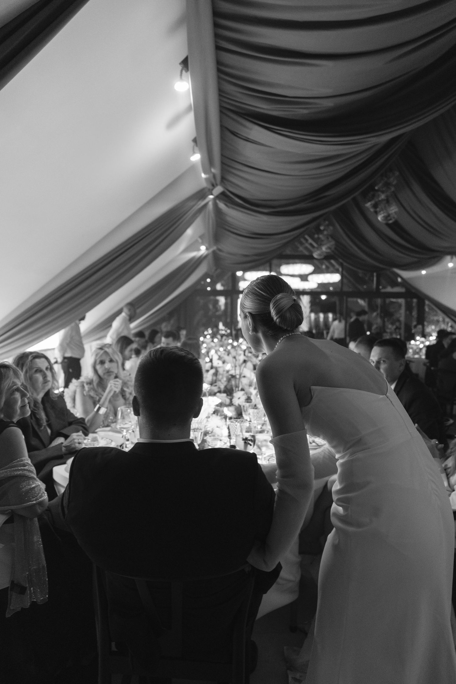 Reception scene under draped tent ceiling with guests gathered at decorated tables.