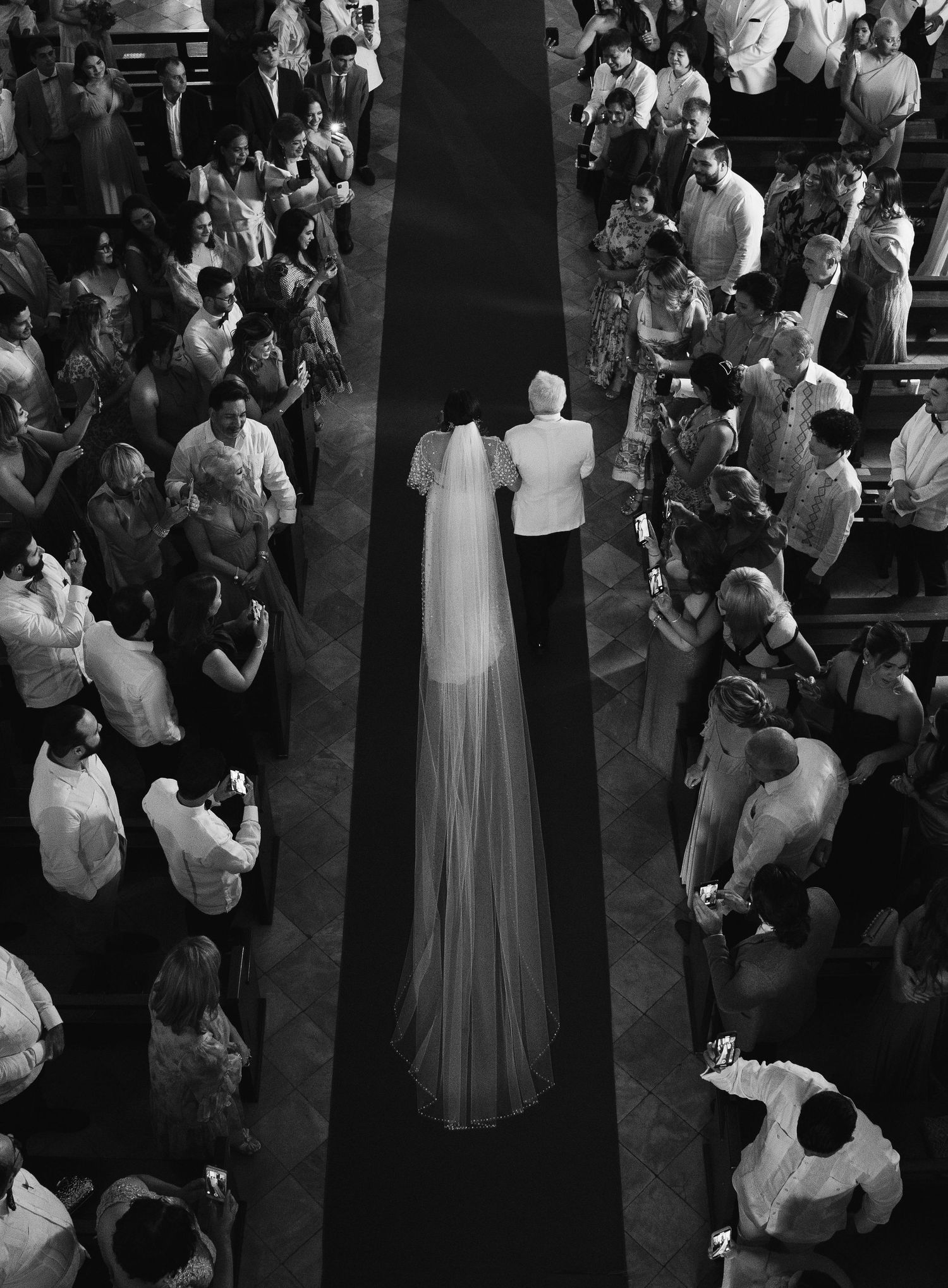 Aerial view of wedding processional in black and white with dramatic veil perspective.