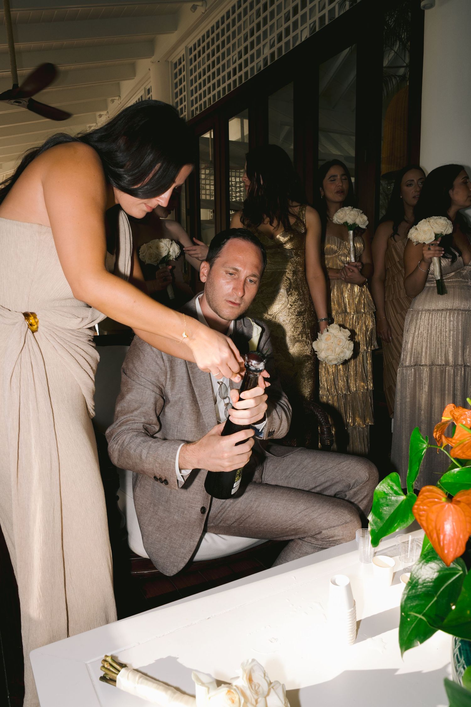 A couple in formal attire signs documents at a wedding ceremony while guests look on in the background.