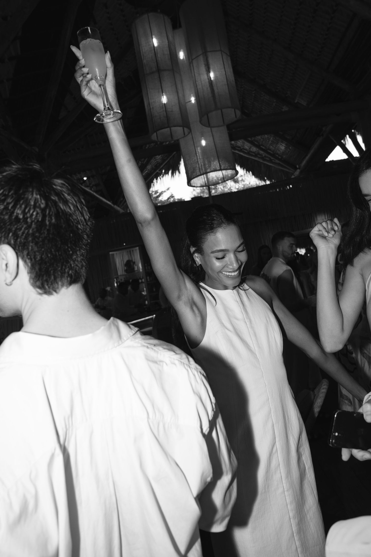 Black and white photo of a crowd dancing and enjoying themselves at a nightclub under chandelier lighting.