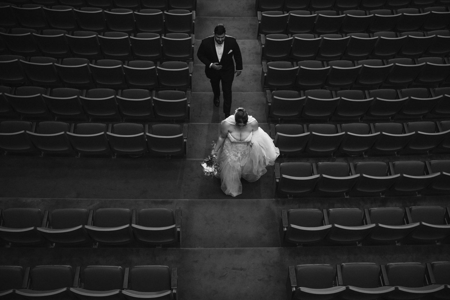 Artistic black and white photo of a couple walking through empty theater seating.