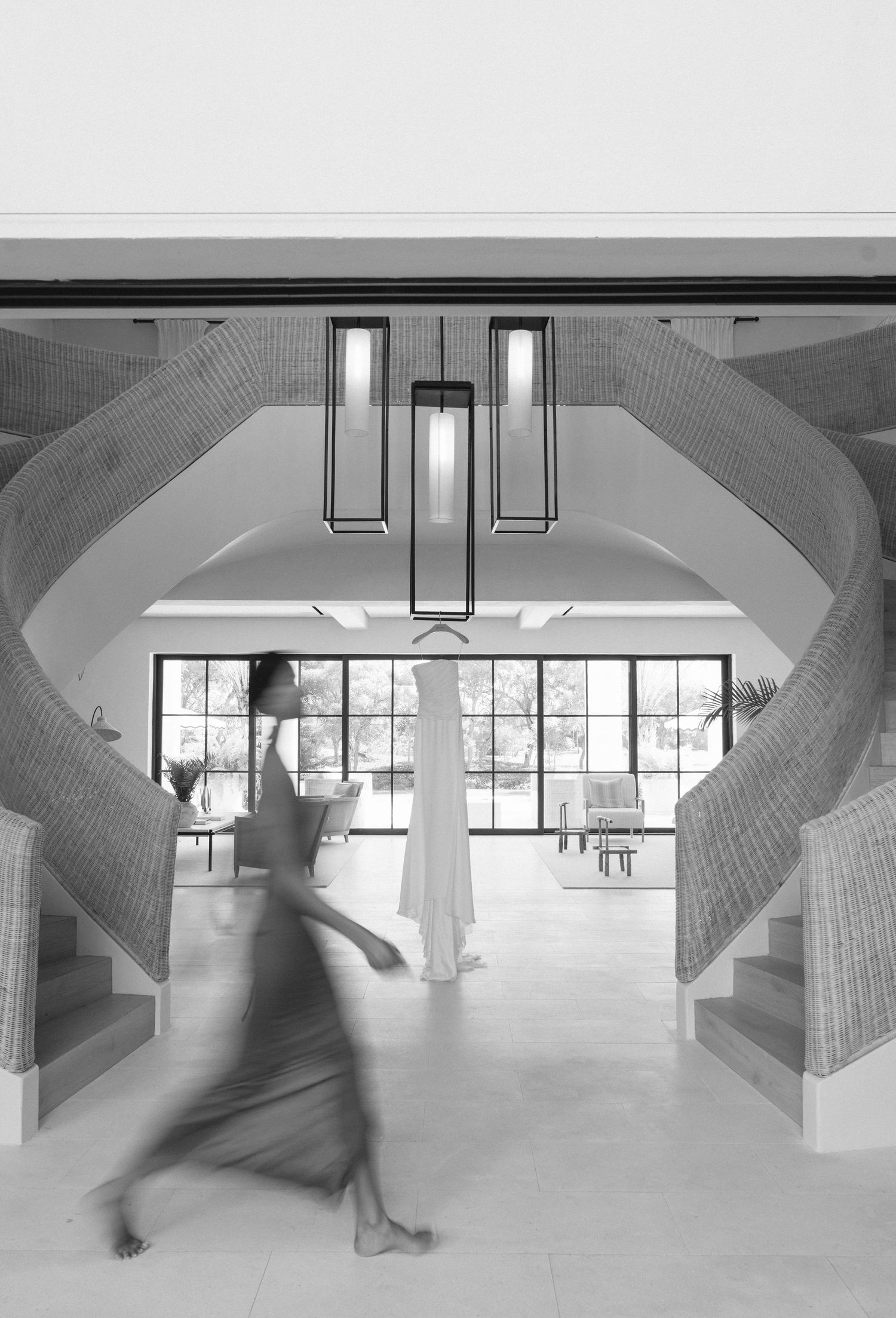 Black and white architectural photo showing a modern interior with curved staircases and hanging pendant lights.