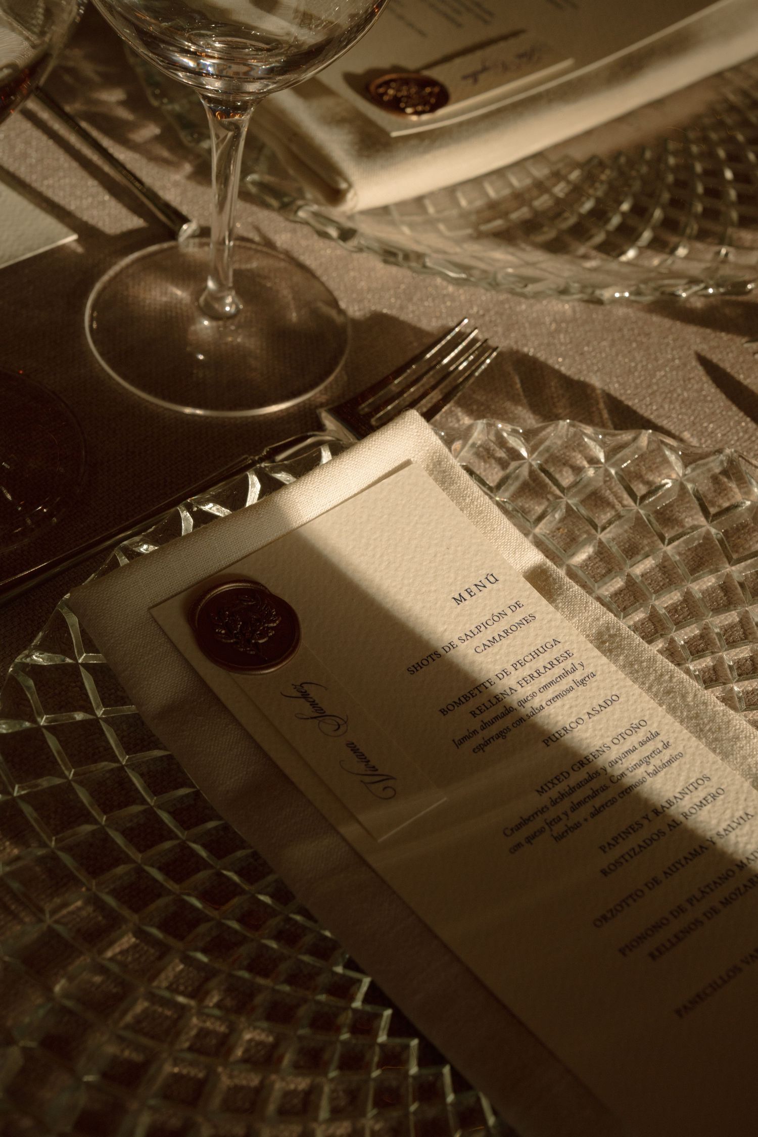 A wedding menu card and wine glass on a textured tablecloth in sepia tones.
