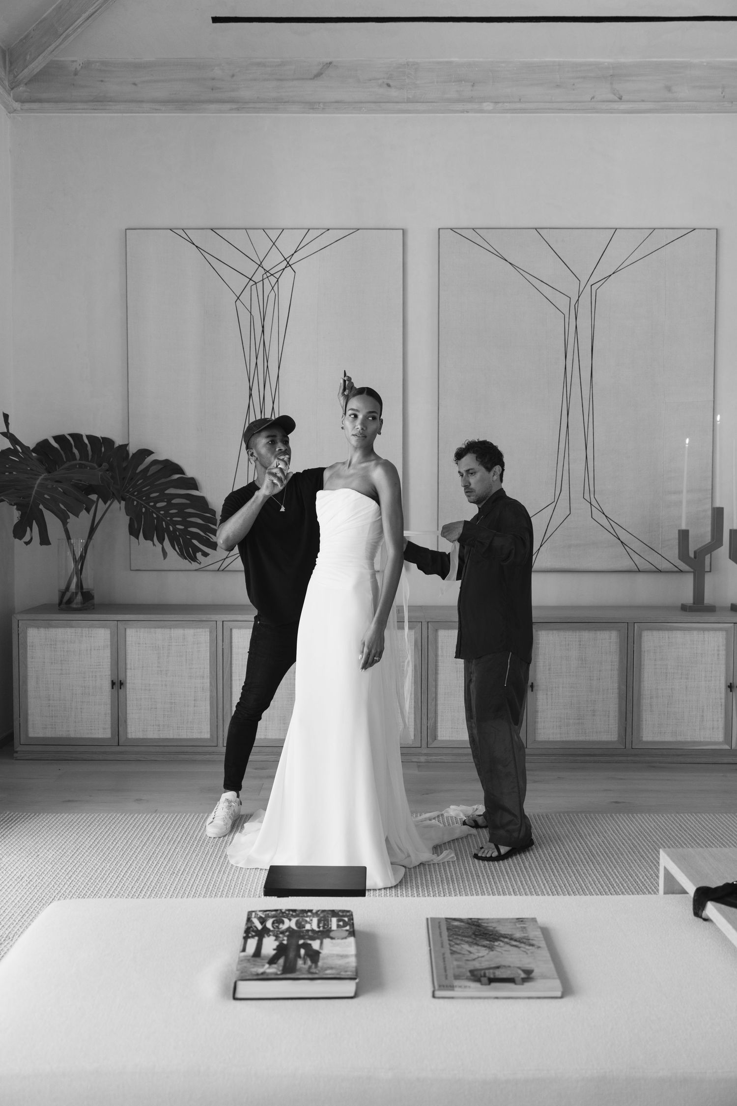 A black and white photo sequence showing a white dress being arranged on a table with wall artwork in the background.