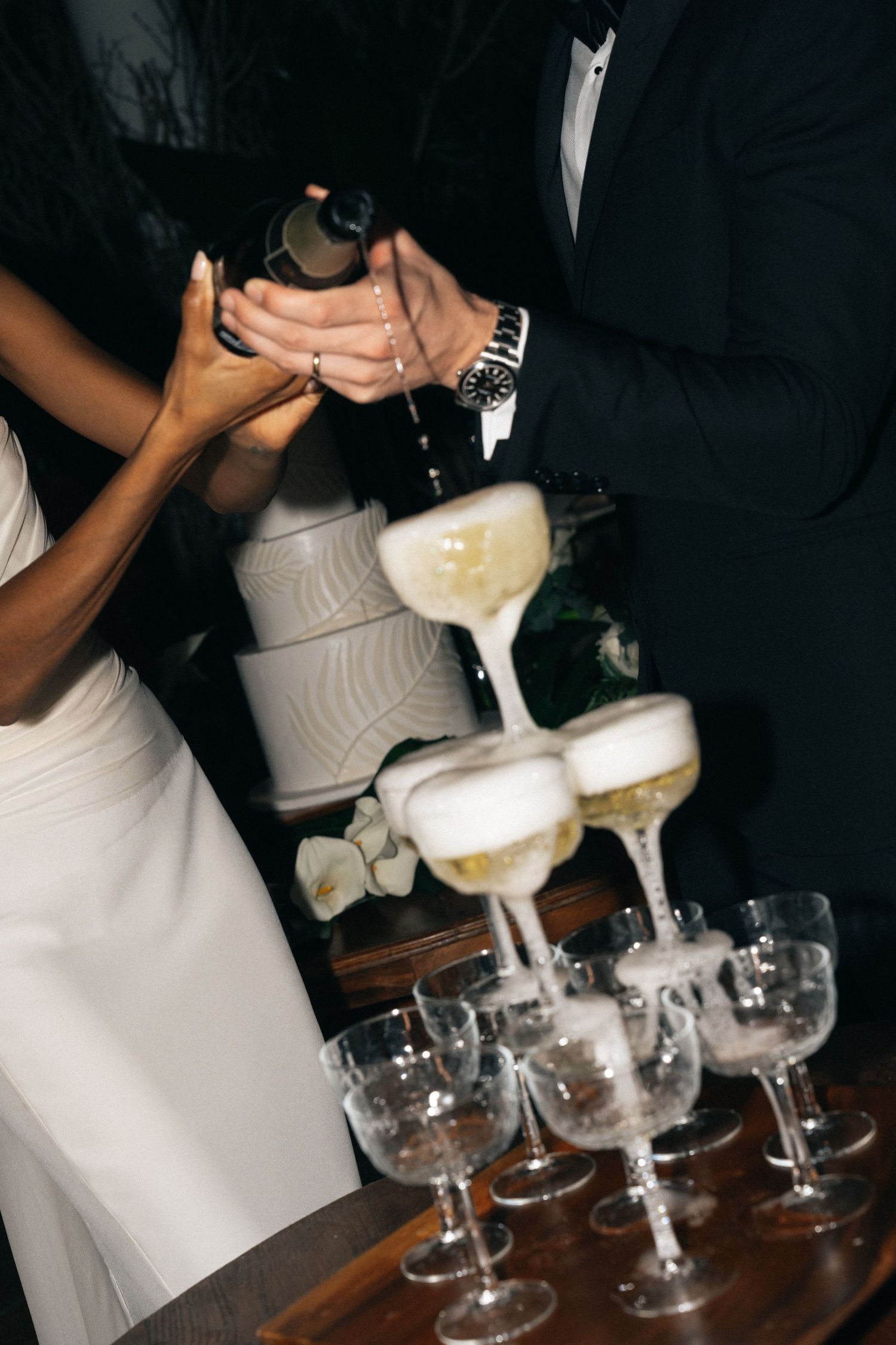 Champagne being poured into a tower of coupe glasses at an elegant celebration.