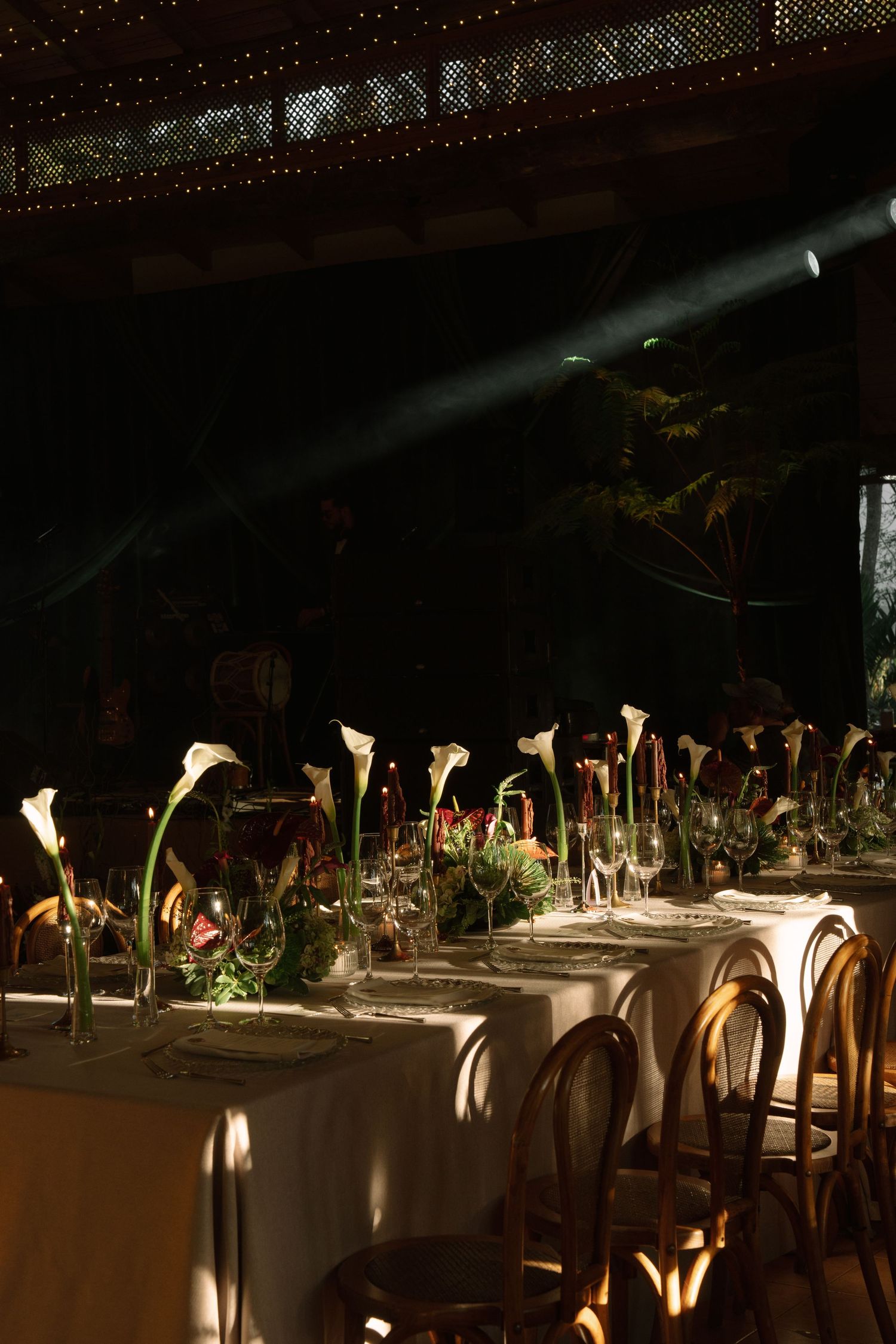 Elegant wedding reception table set with white calla lily centerpieces and bistro chairs in dark venue.