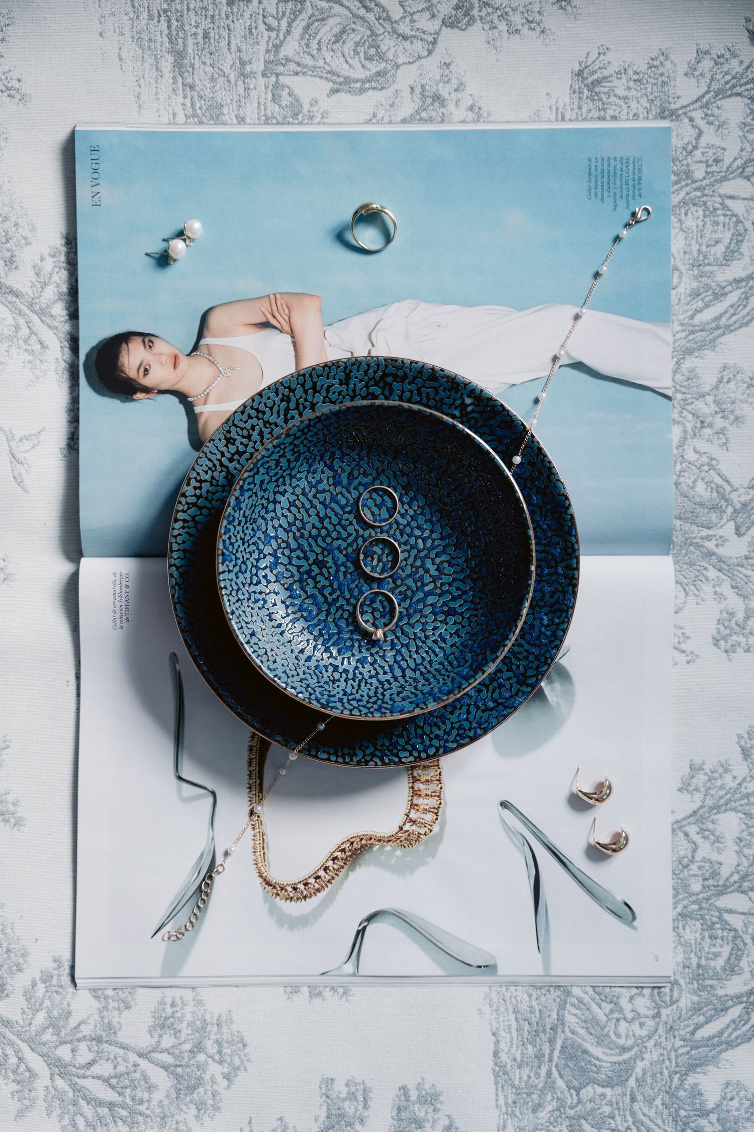 Editorial style flatlay featuring a blue decorative plate with jewelry and accessories.