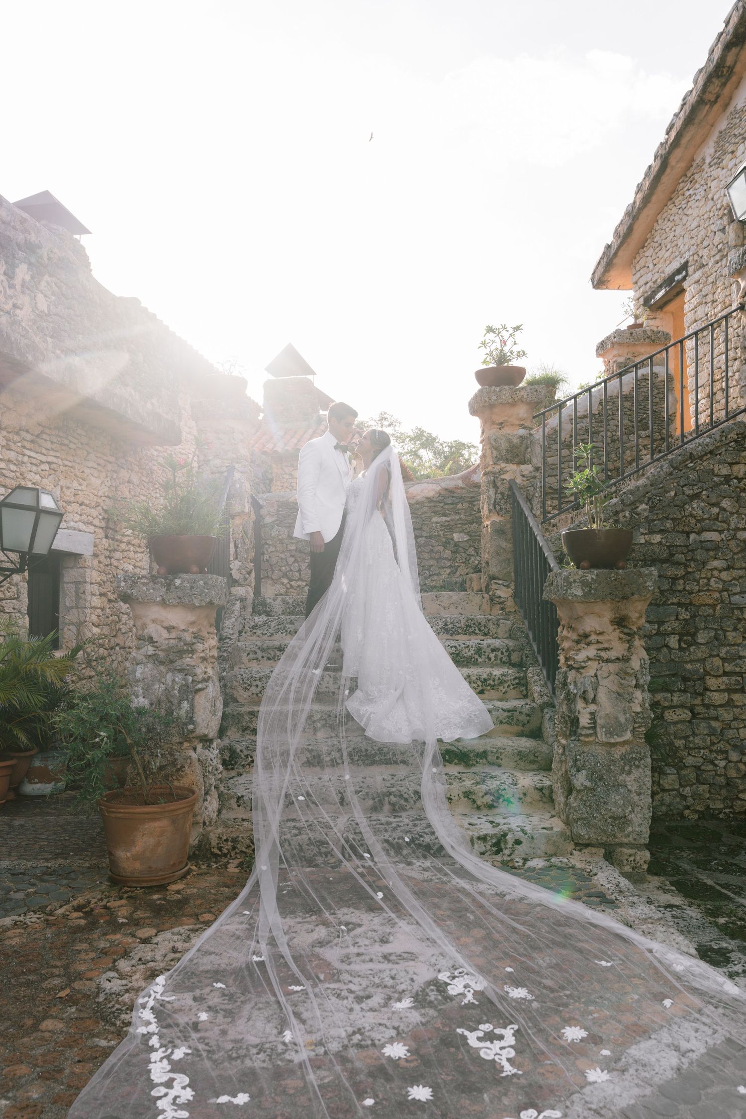 Long cathedral veil trailing down rustic stone steps in golden sunlight.
