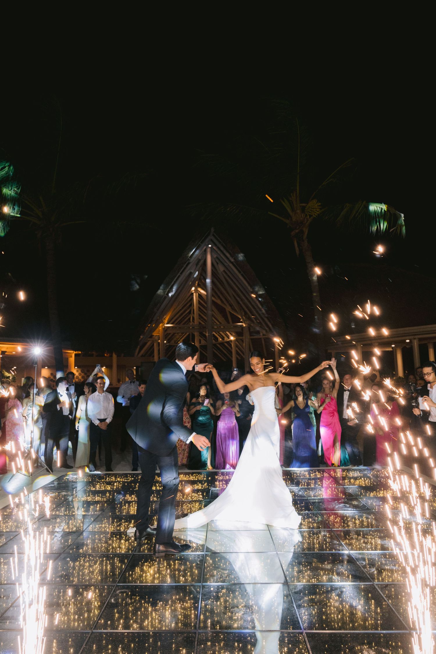 Wedding celebration at night with sparklers illuminating a dance floor as party guests celebrate under dark sky.