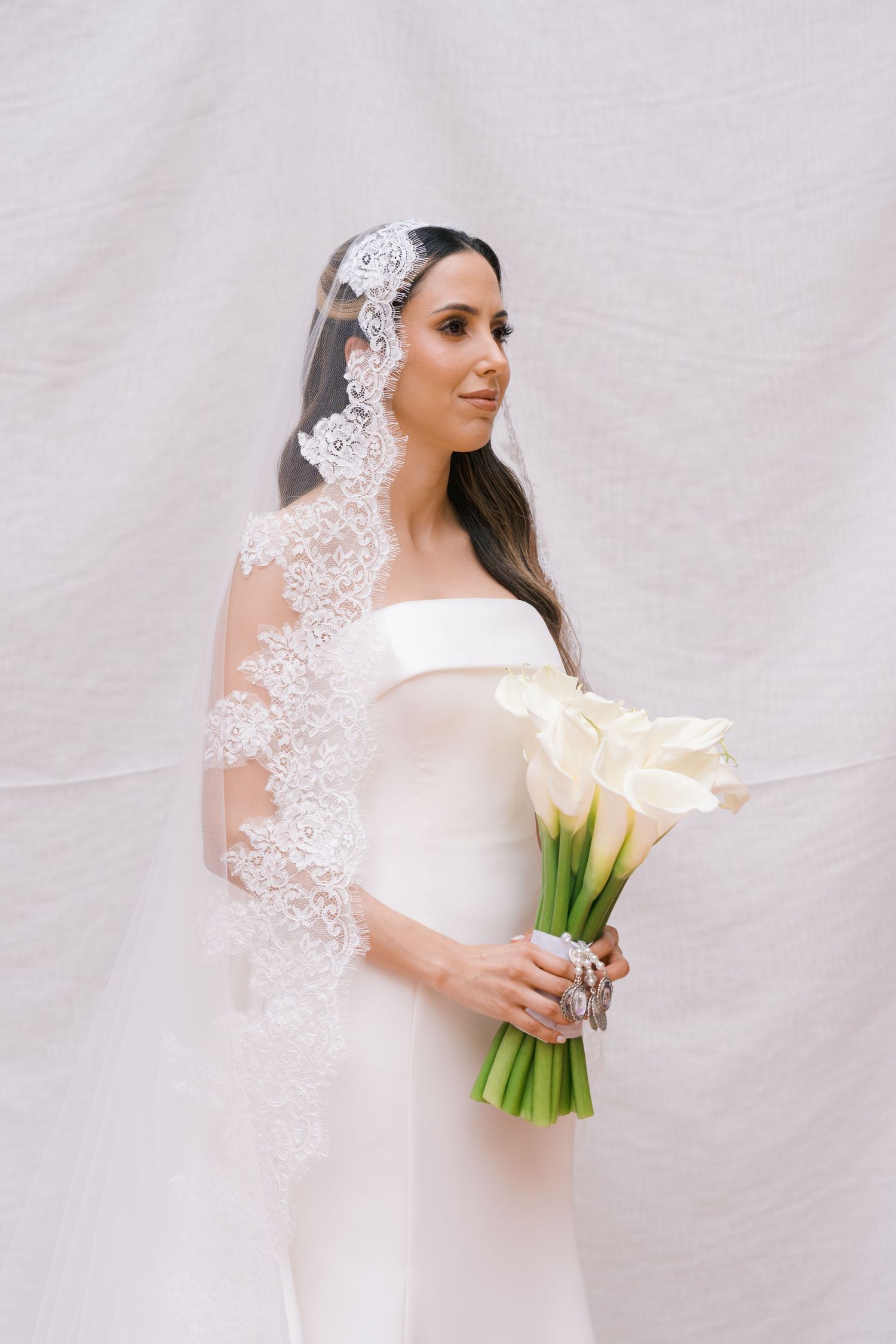 Classic bridal portrait featuring off-shoulder gown, lace veil, and white calla lily bouquet.