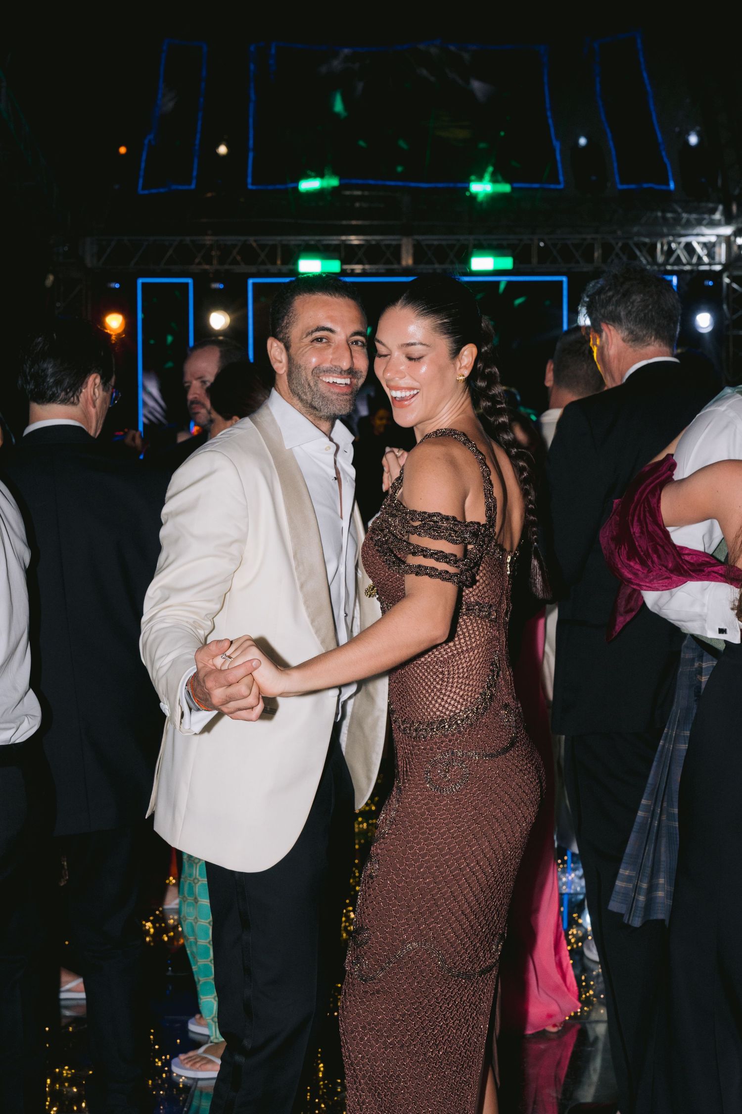 Couples dancing together at a formal event with dramatic stage lighting and decorative elements in the background.